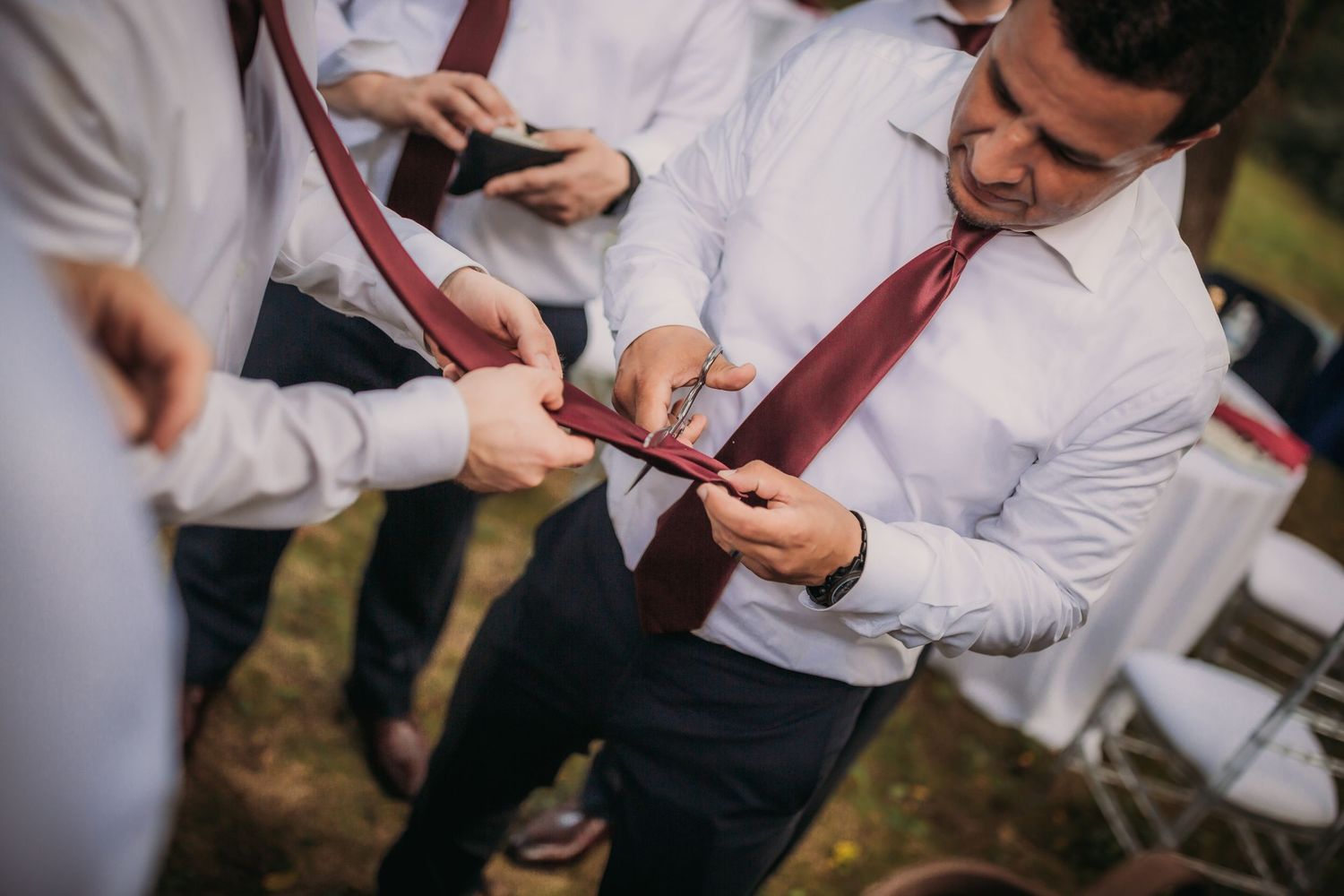 Wedding party members in coordinated red ties and white shirts huddle together outdoors.
