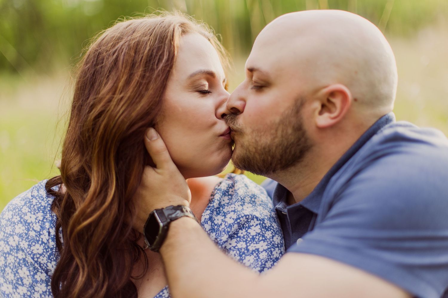 Loving couple shares playful kiss while relaxing outdoors in spring meadow.