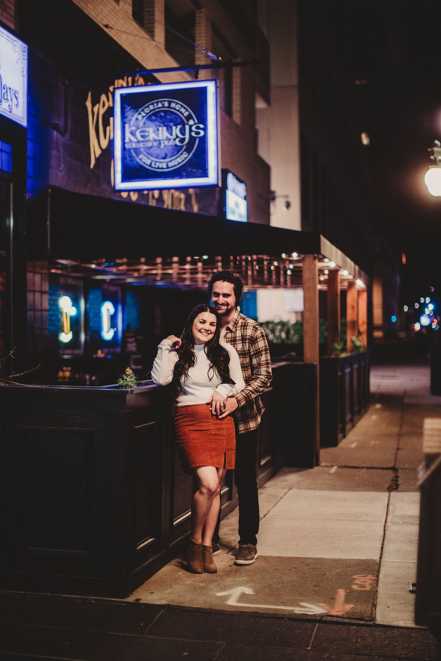 Couple posing outside Kehoots bar at night with neon signage illuminating the scene.