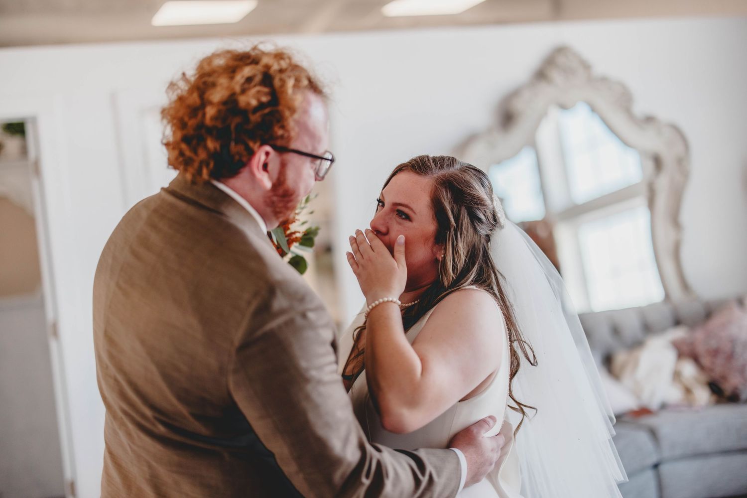 Emotional wedding moment between couple sharing tears of joy in light-filled room.