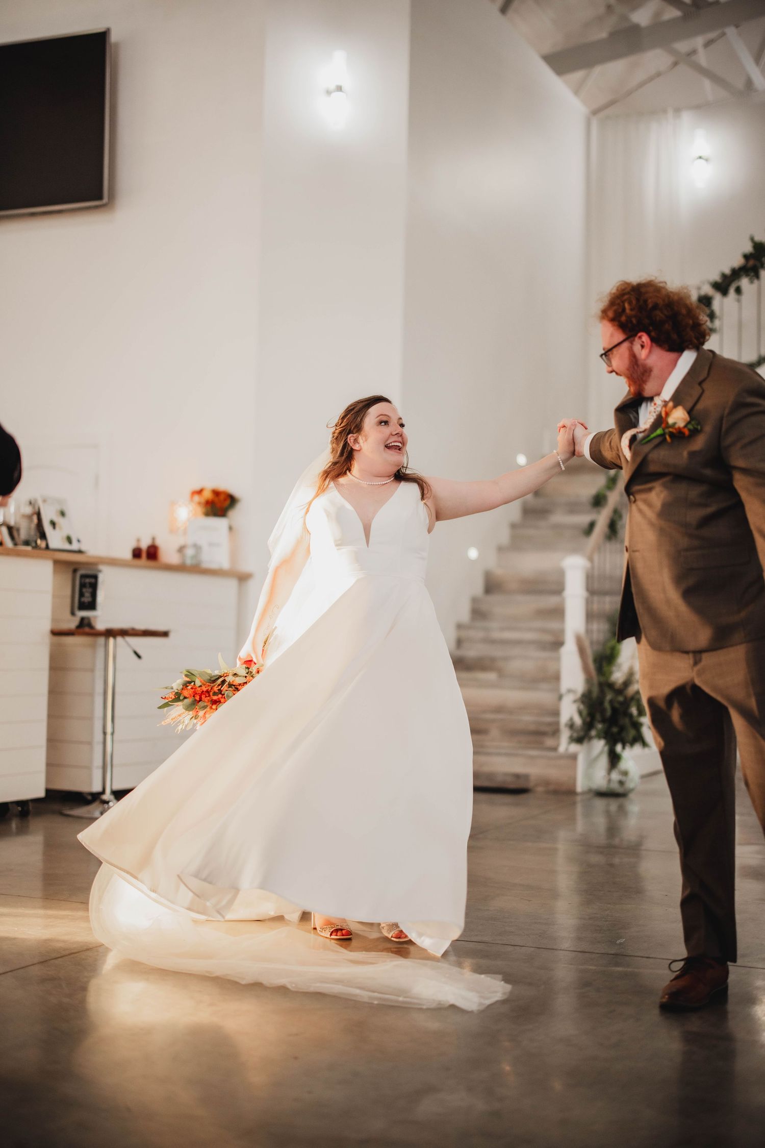 A happy couple dancing and laughing together during their wedding celebration in a bright white venue.