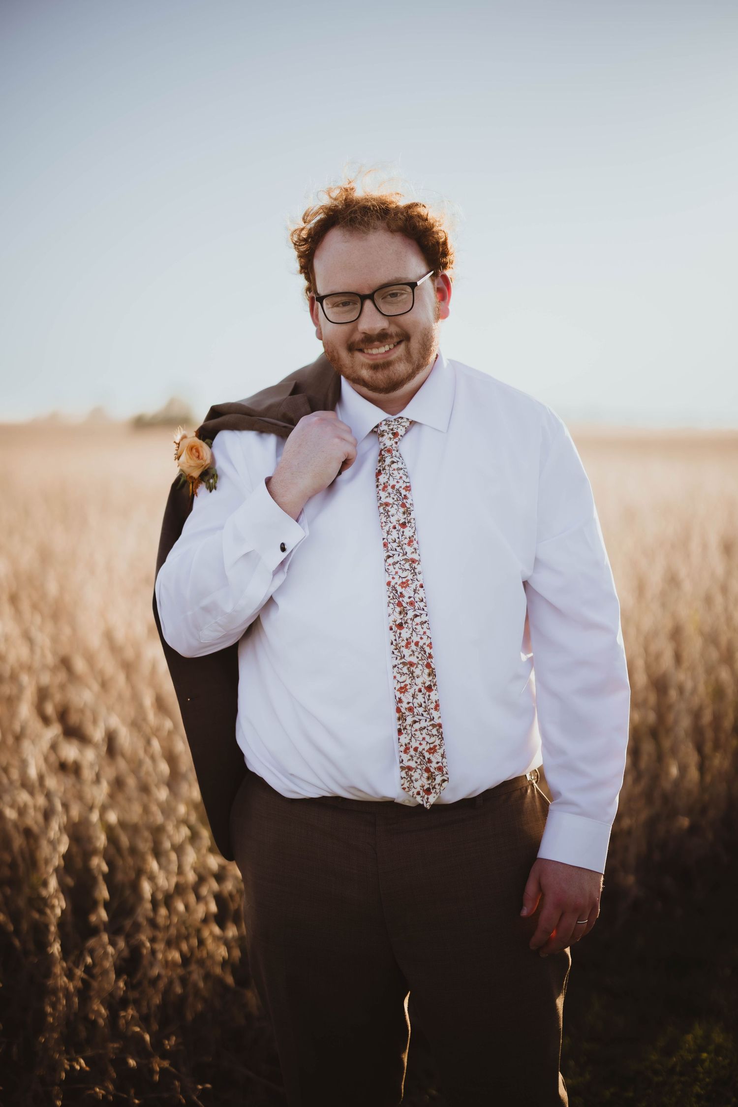 Casual portrait of groom wearing white shirt and floral tie against natural backdrop.