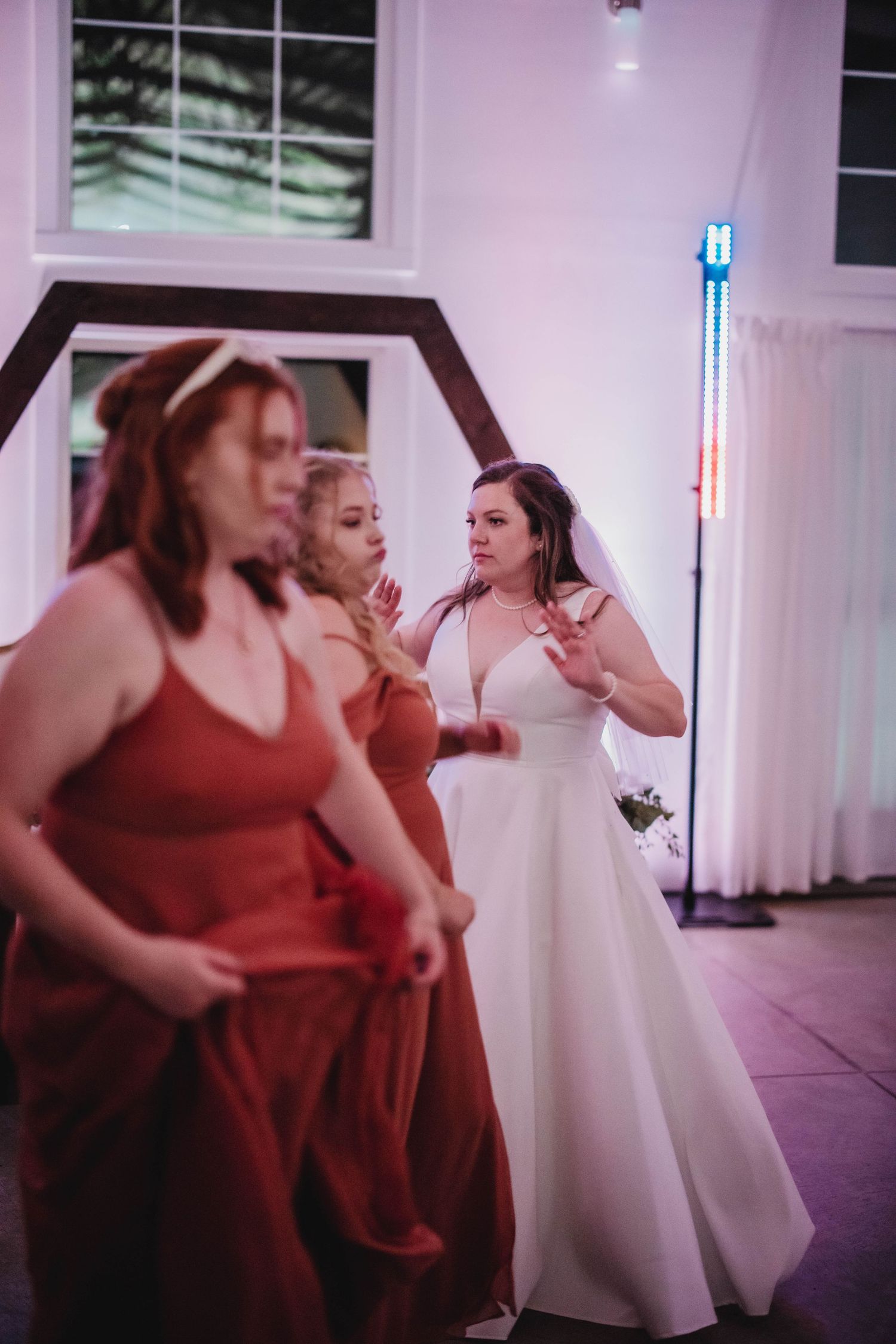 Wedding party members in red dresses dance with the bride at an indoor reception.