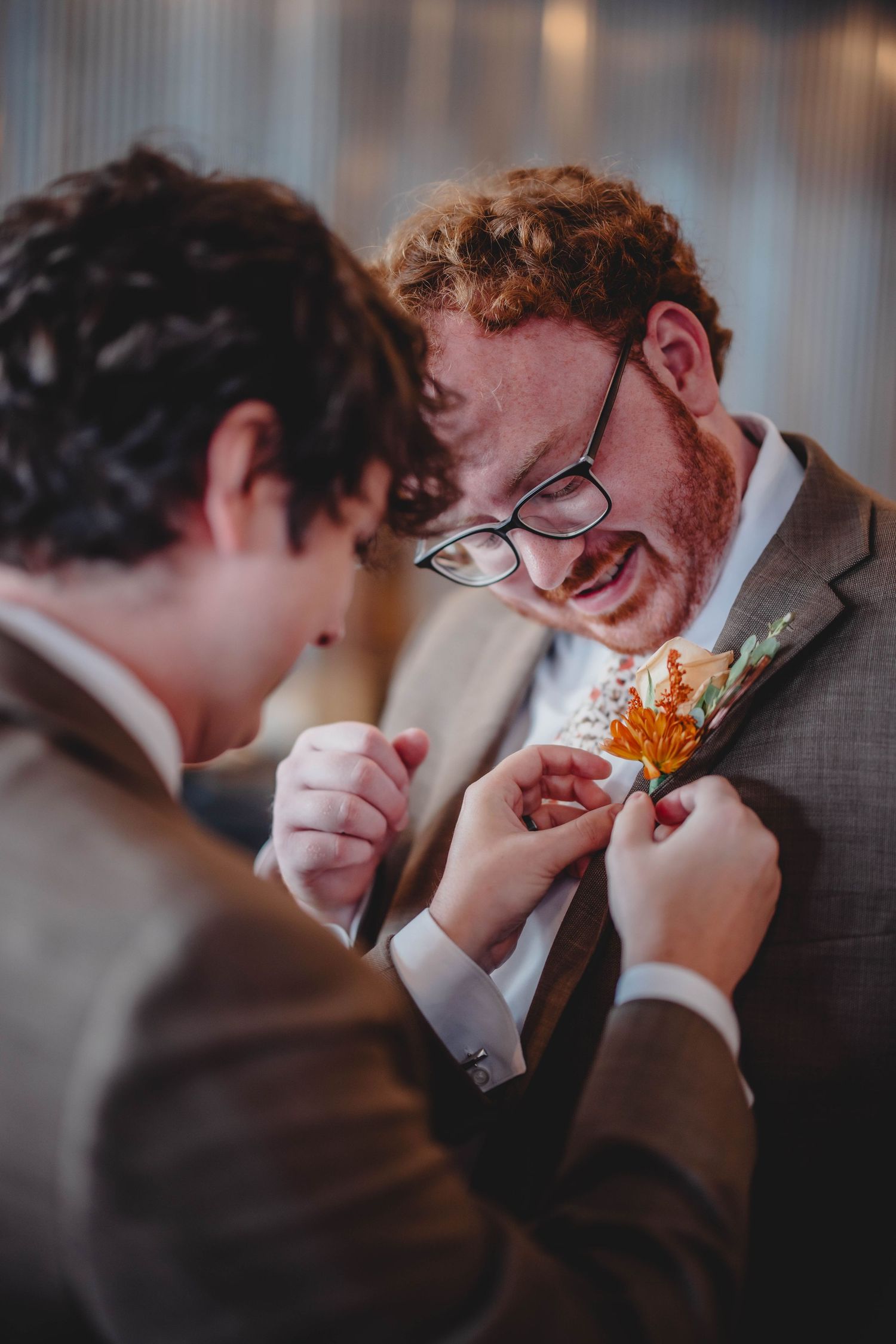 Someone helps adjust a boutonniere on a suit lapel during wedding preparations.