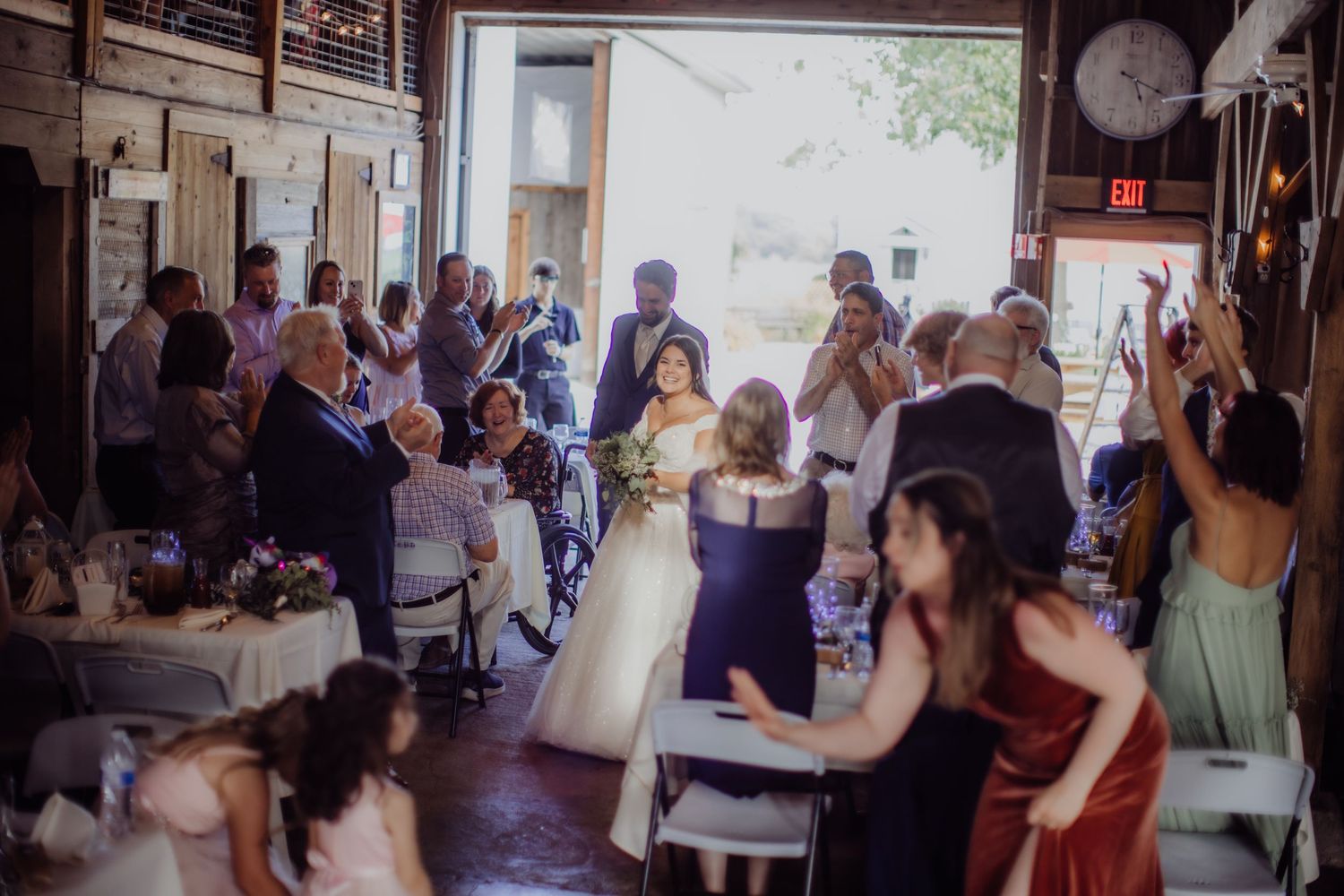 Wedding reception gathering inside a traditional barn with festive lighting and decorations.