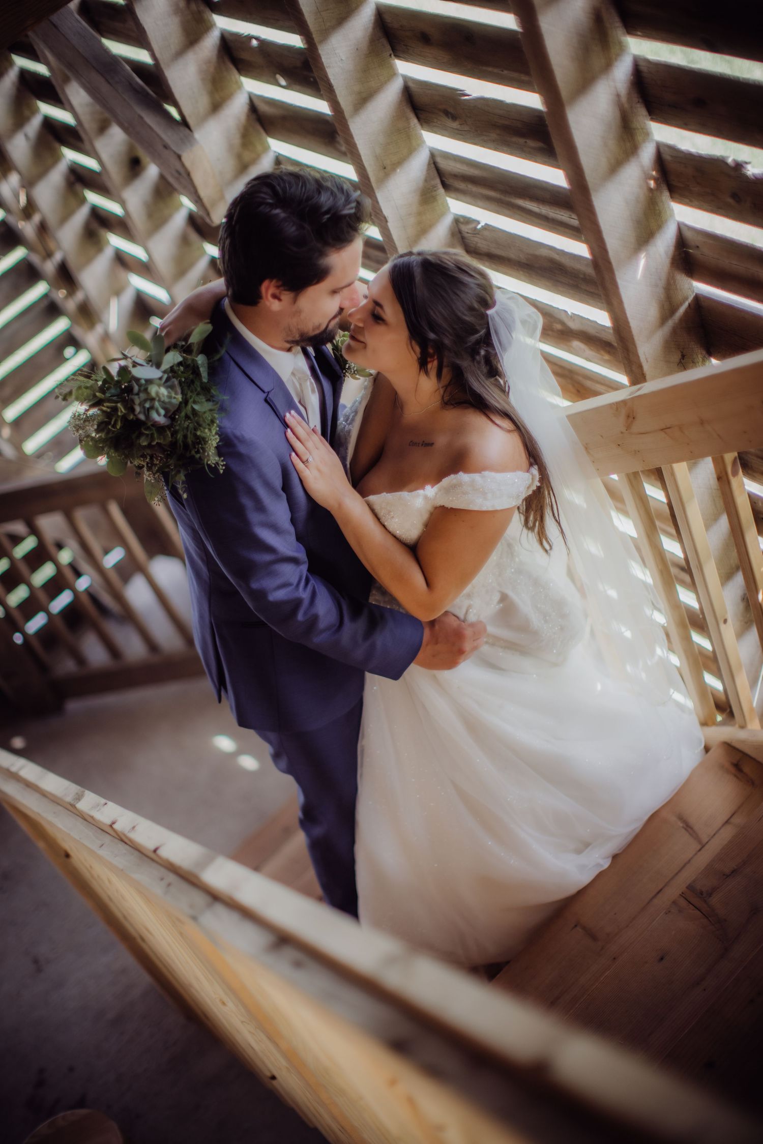 Romantic wedding couple embraces on wooden staircase with geometric lighting patterns.