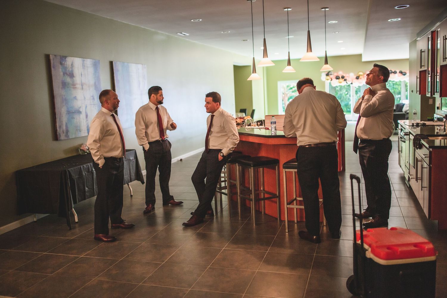 People in formal wear socializing near modern kitchen counter with pendant lighting.