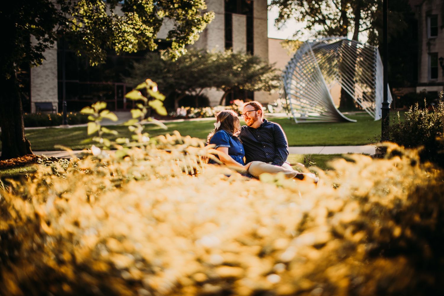 A couple sits together on campus grounds with autumn foliage in the foreground.