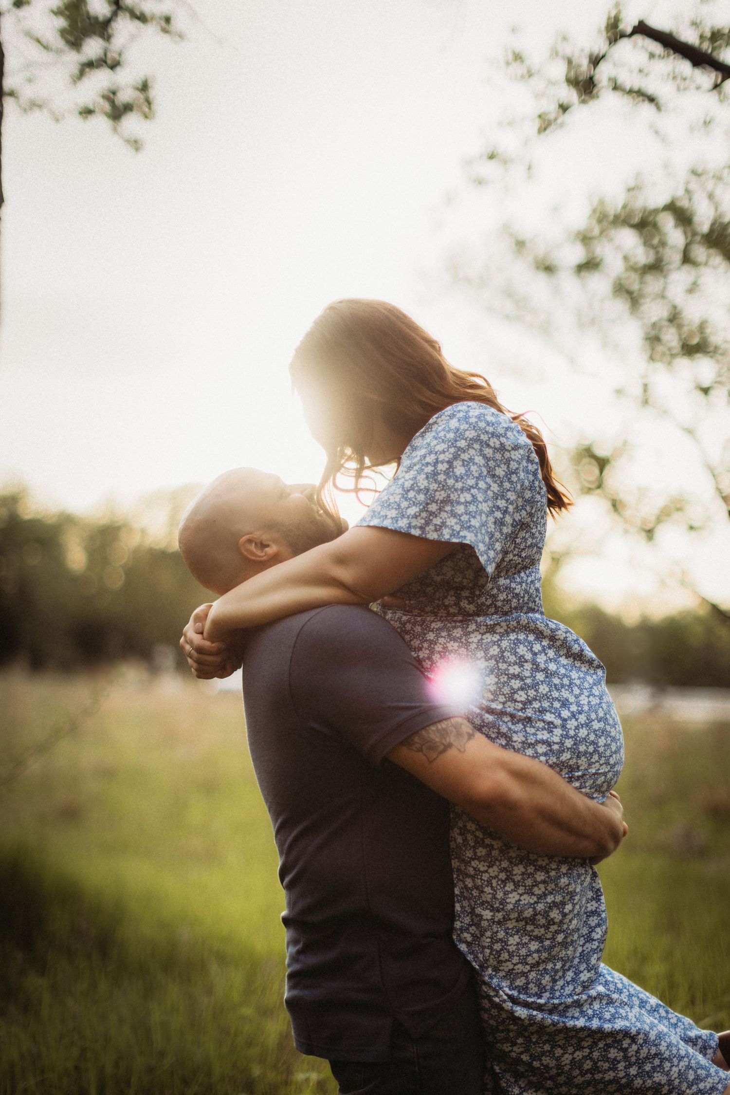 Romantic sunset portrait of a couple embracing with backlit glow in a field.