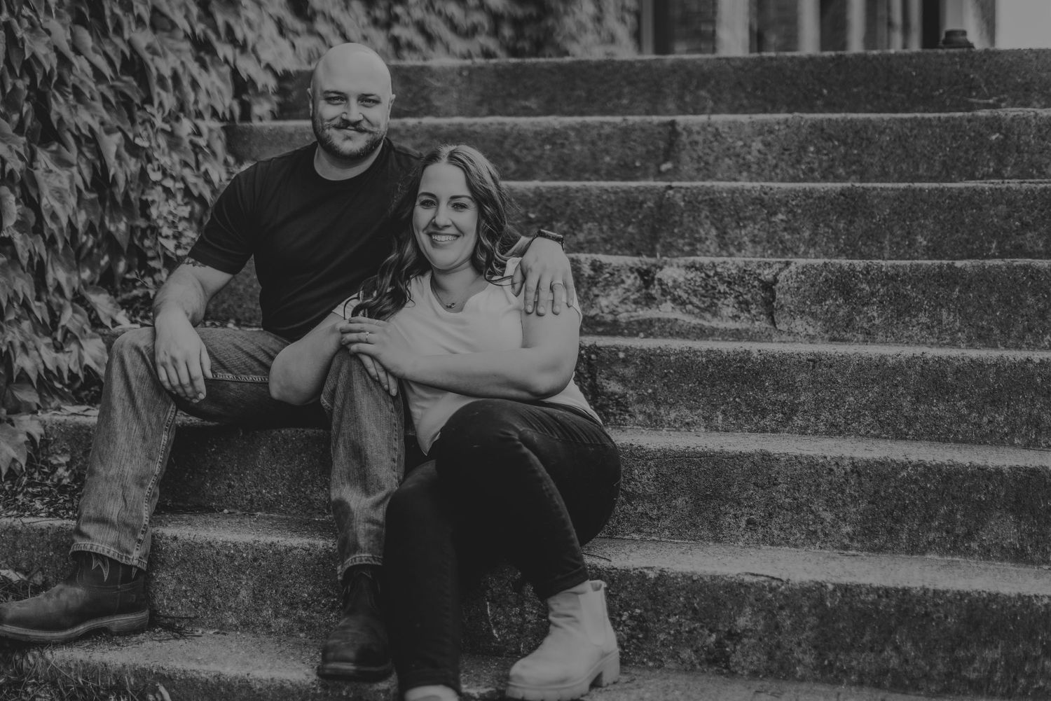 Black and white portrait of couple sitting together on outdoor stone steps.