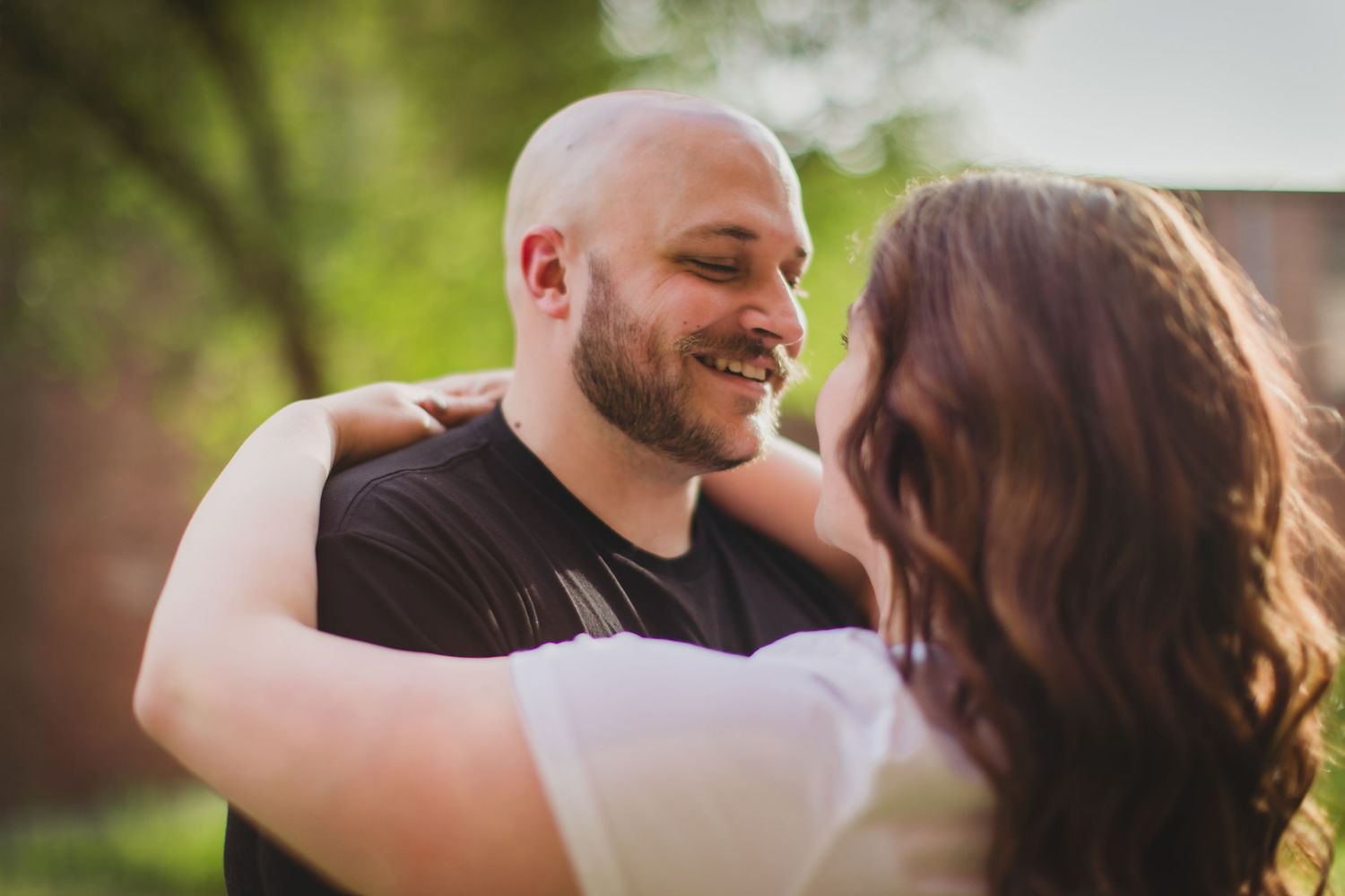 A joyful couple laughs together while embracing outdoors in natural lighting.