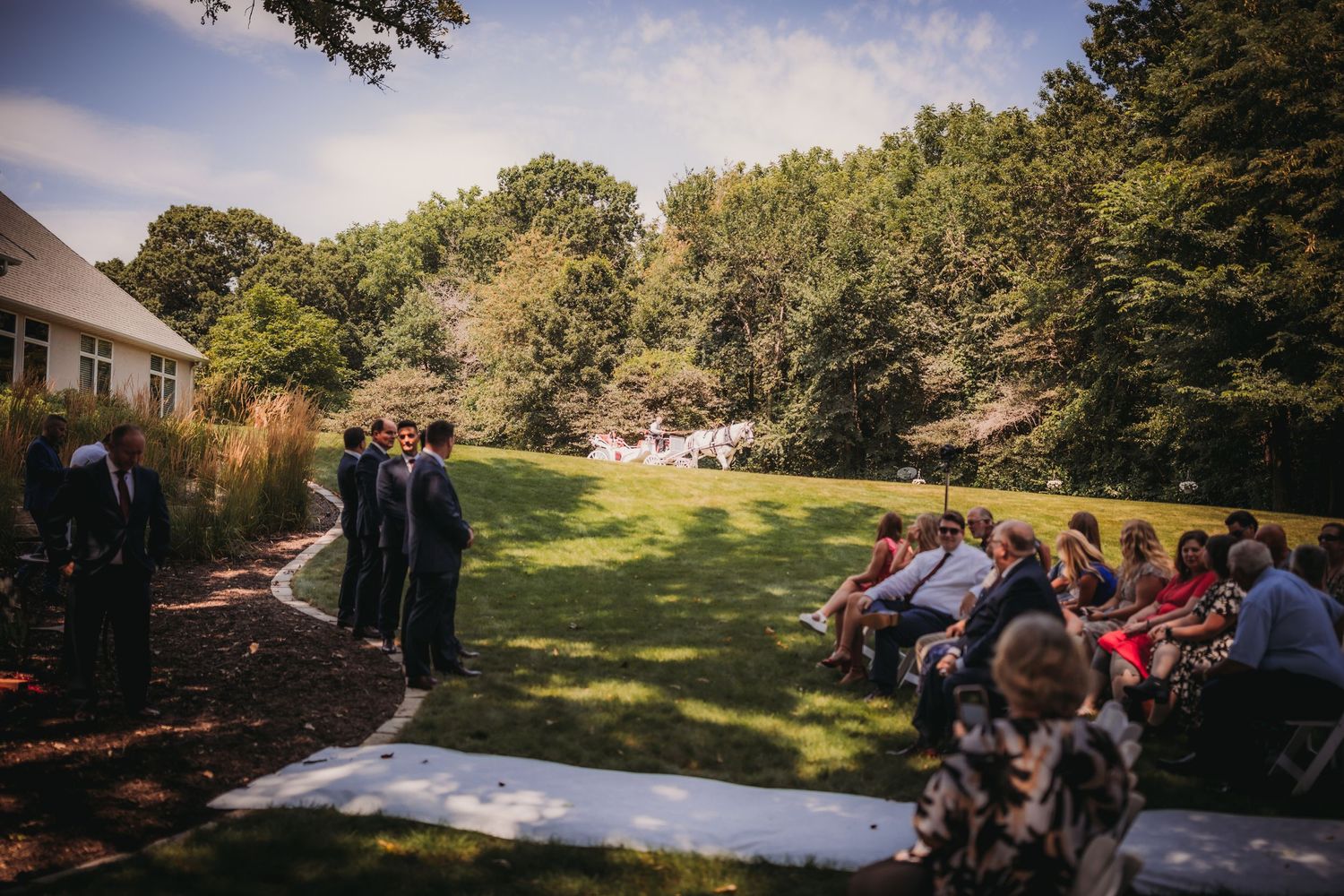 Wedding guests seated on white chairs at an outdoor ceremony near a large building.