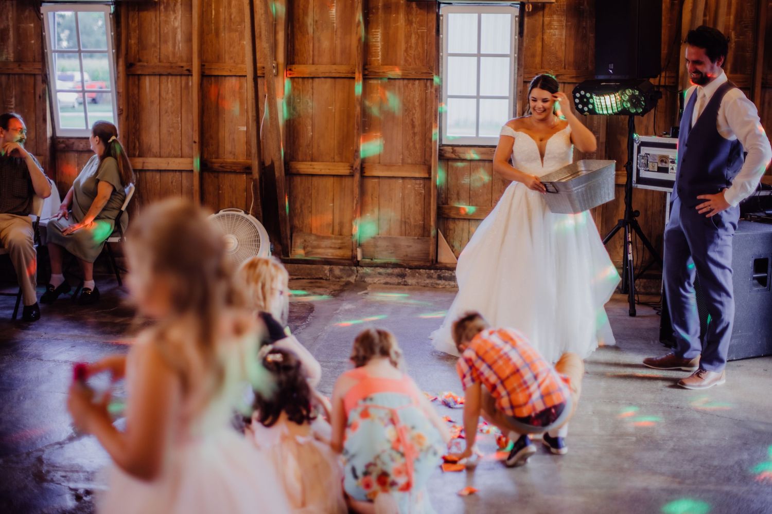 Reception guests dancing and celebrating on a barn dance floor with colorful lighting effects.
