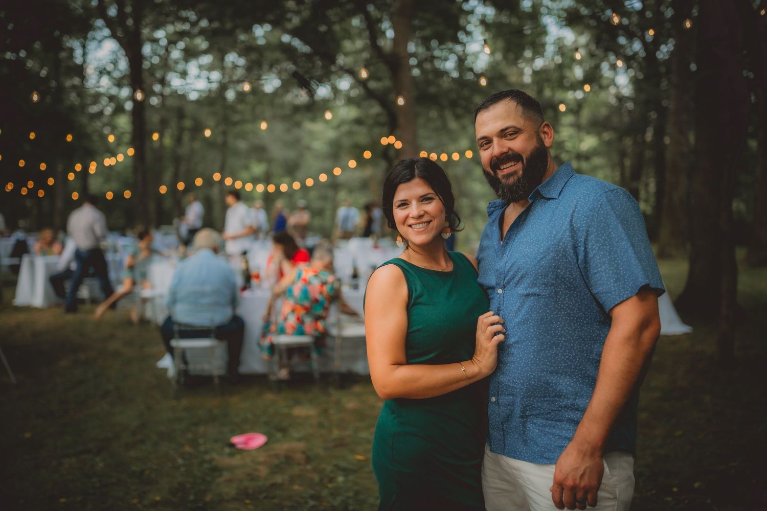 Outdoor evening celebration with string lights illuminating guests in a wooded setting.