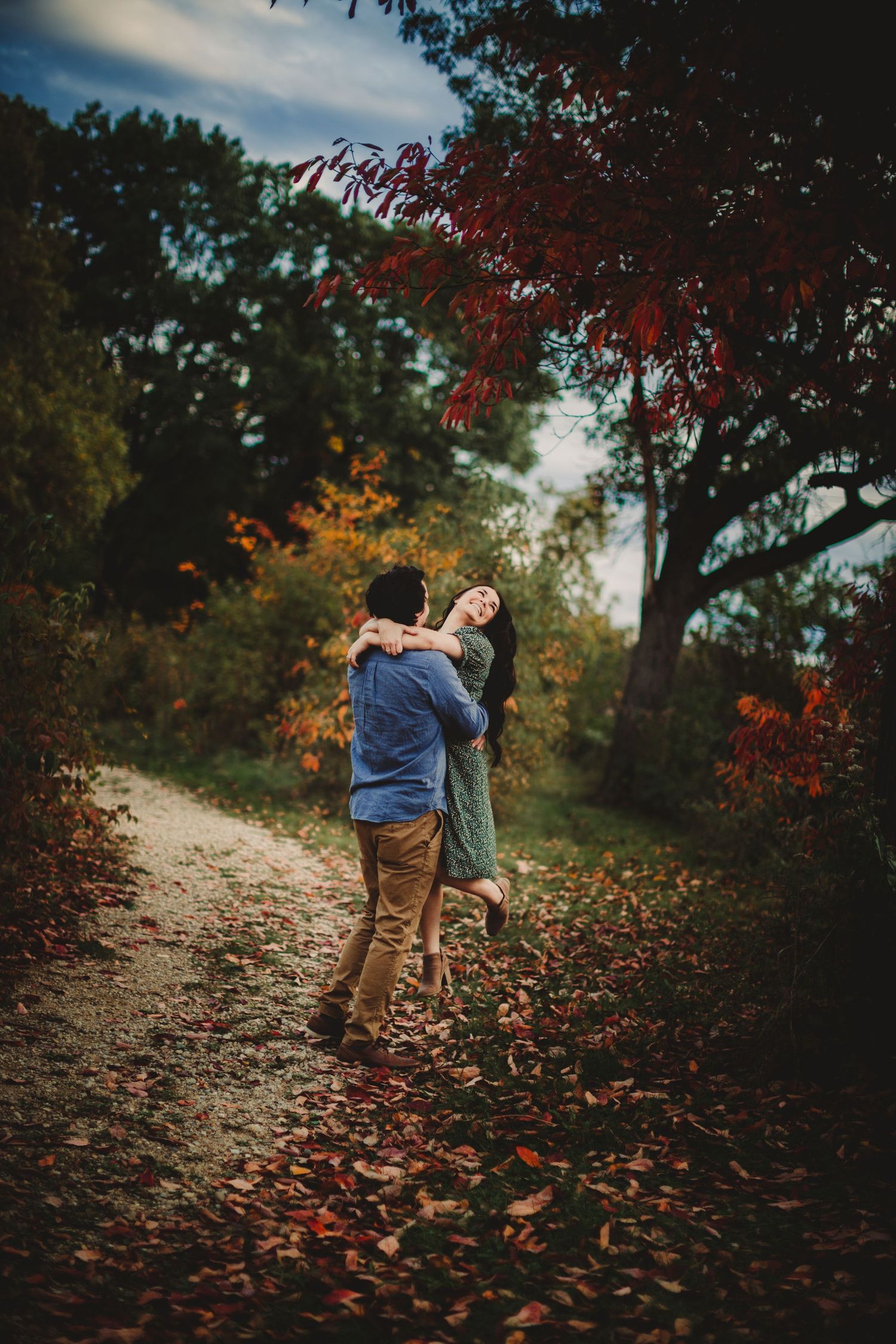 Couple embraces on autumn trail surrounded by colorful fall foliage.