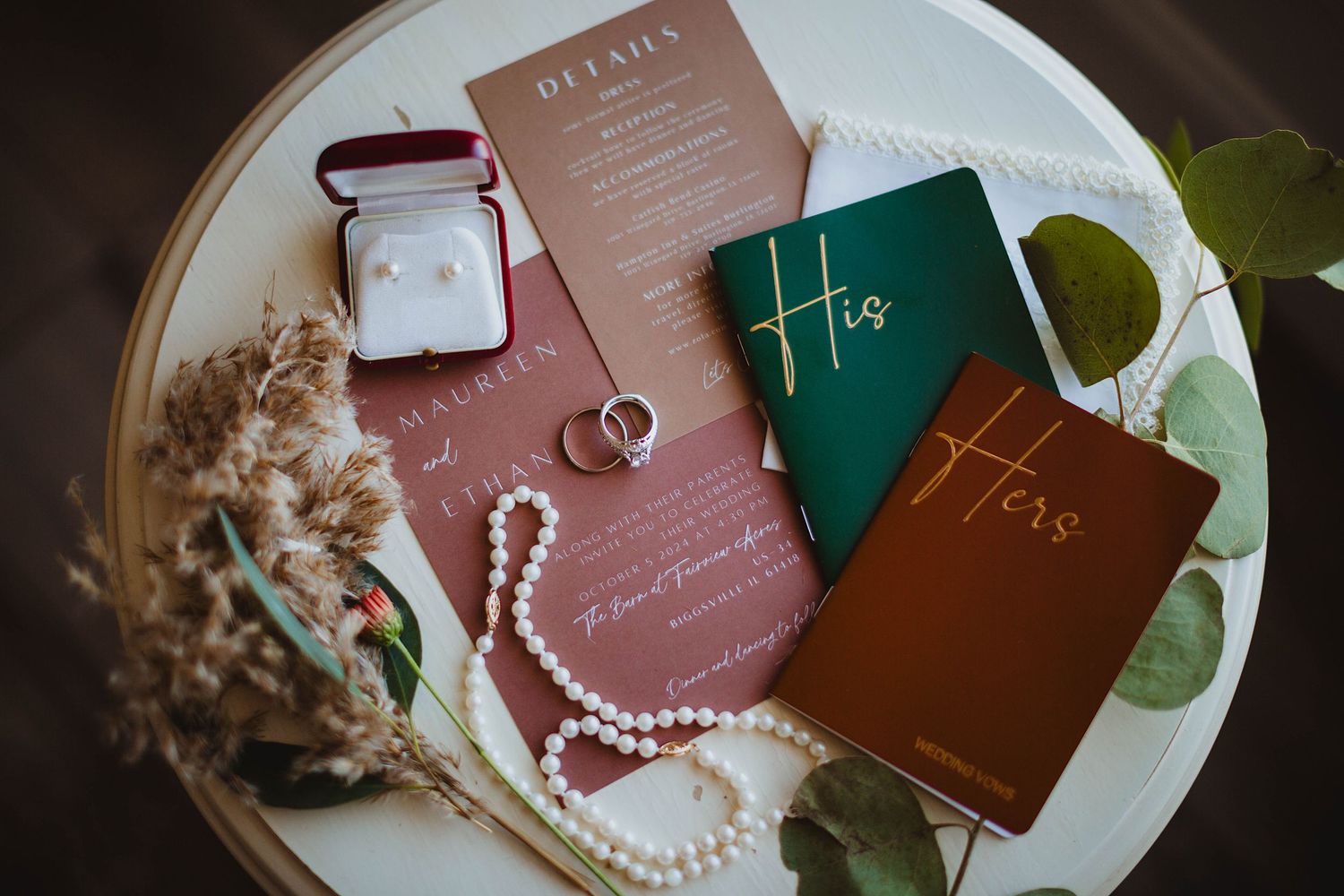 Wedding invitation suite with rings and vow books arranged on white ceramic plate.