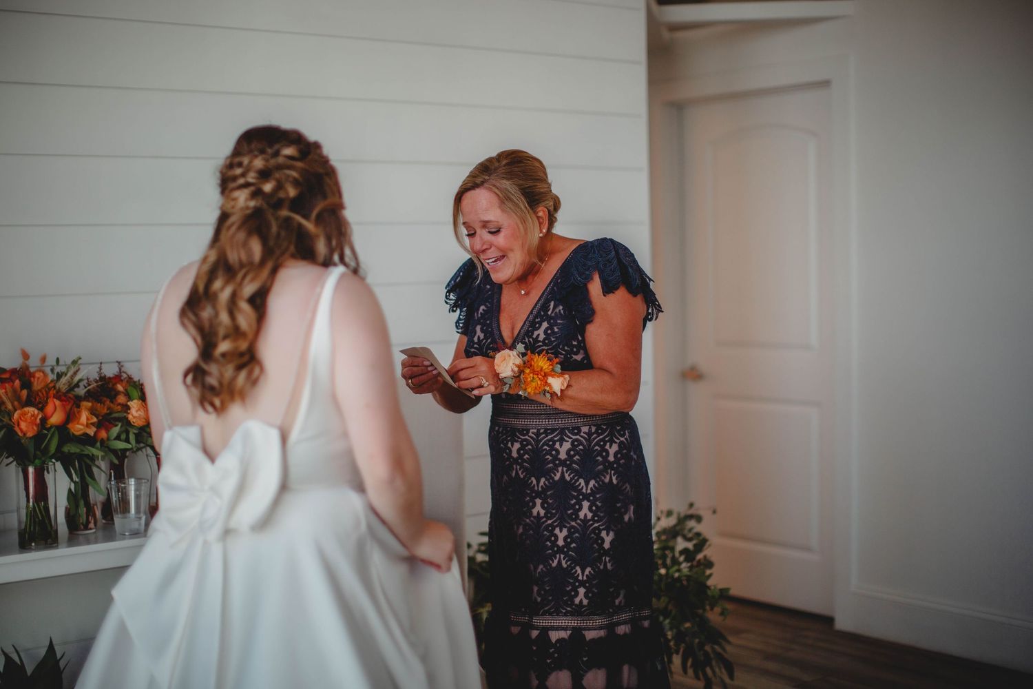 Two people share an emotional moment during wedding preparations in a white-walled room.