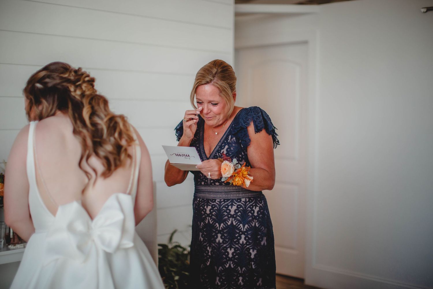 Someone in a navy dress reads a note while standing with a bride in a white gown.