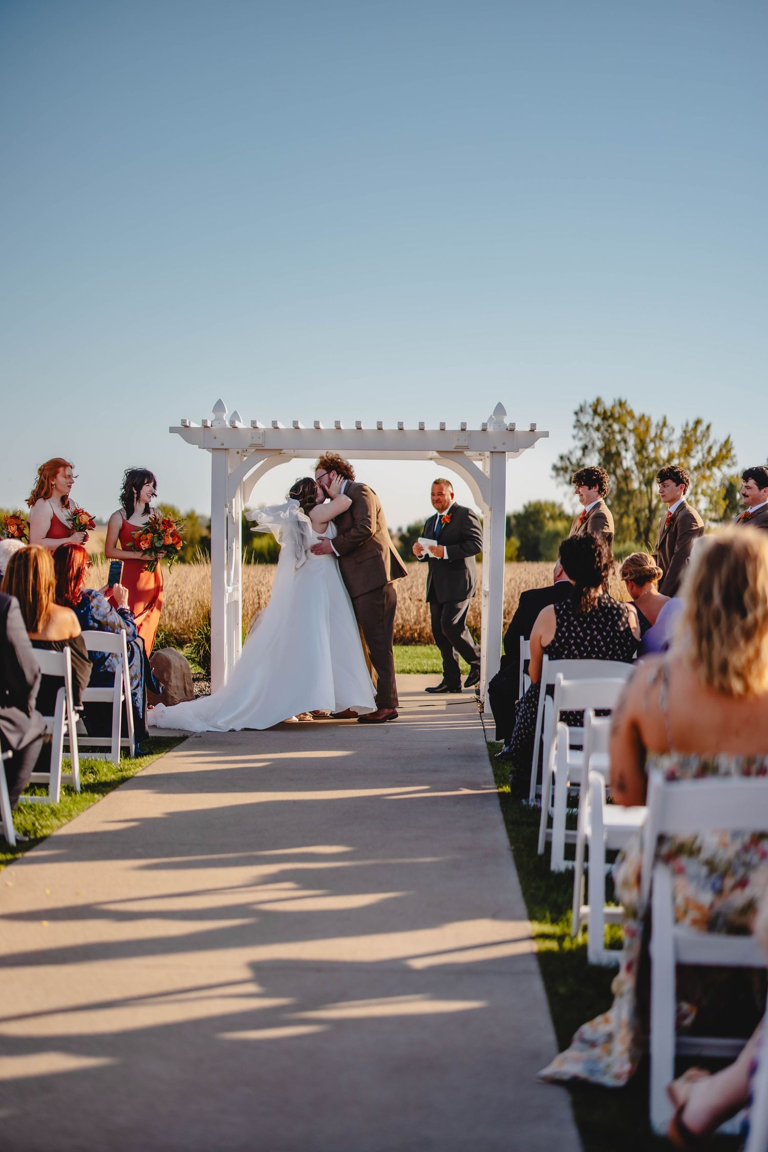 Sunset wedding ceremony with couple embracing under white pergola structure.