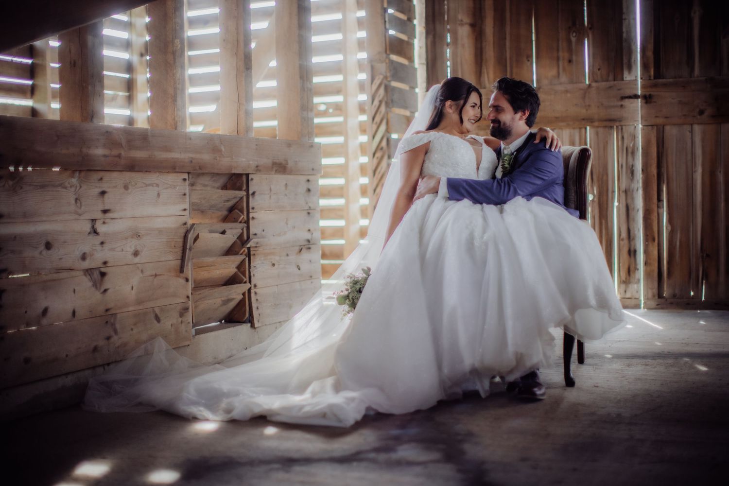 Romantic wedding couple shares intimate moments in a rustic barn setting with natural light streaming through wooden slats.