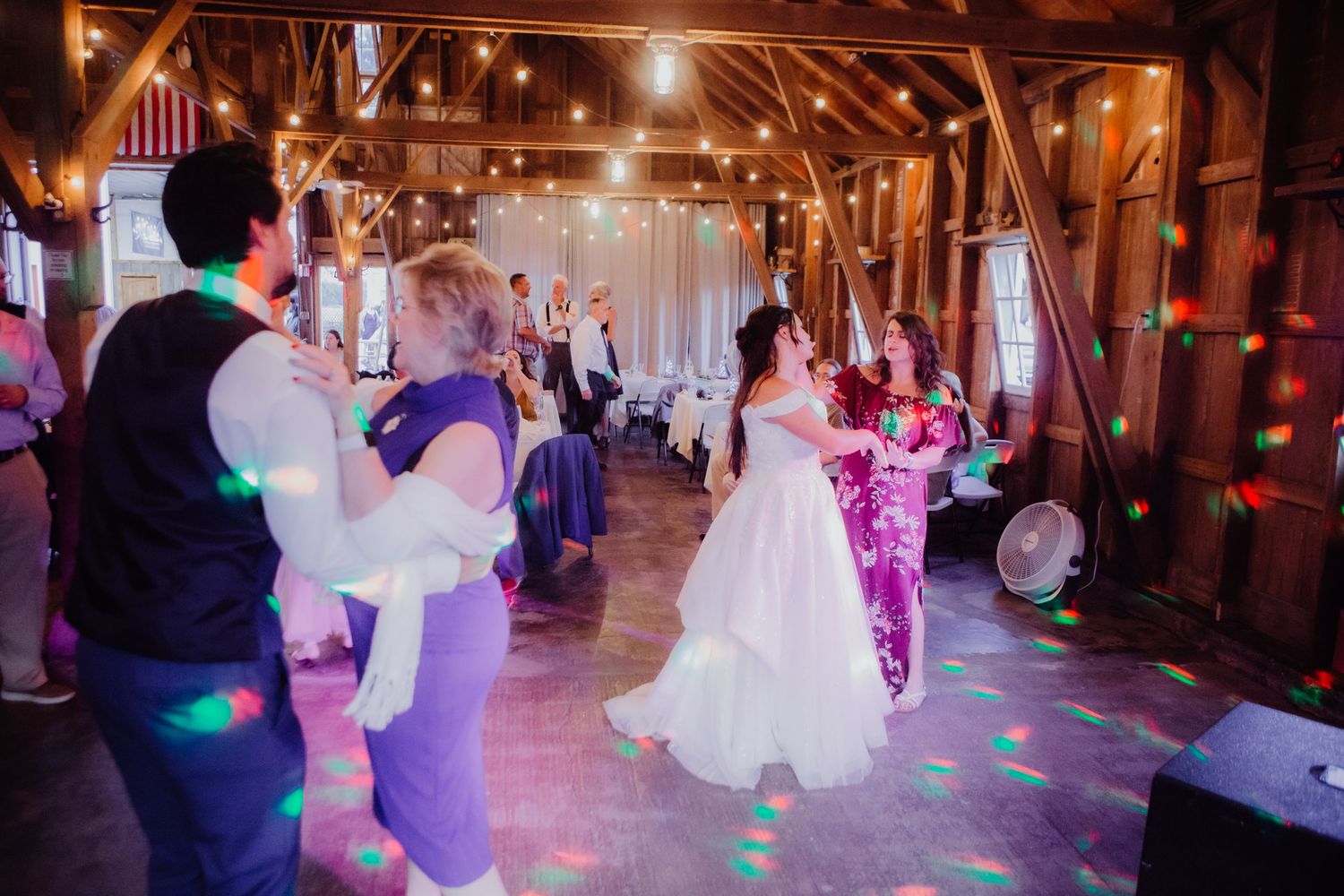 Wide view of a barn wedding reception with guests dancing under string lights.