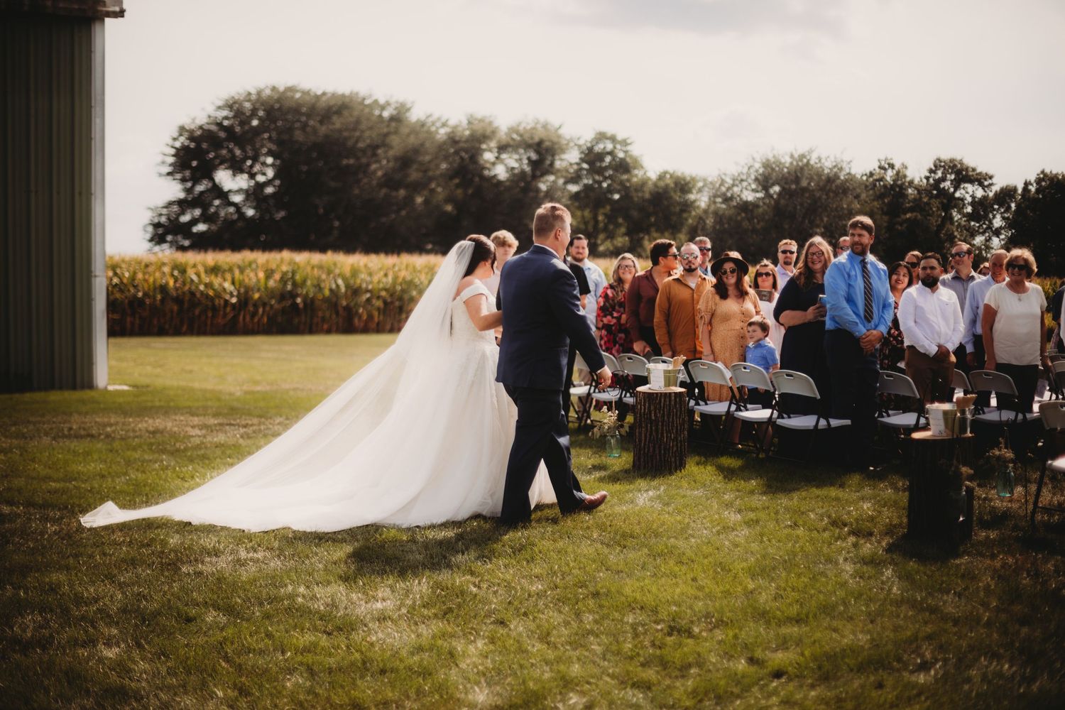 Wedding couple exits ceremony while guests seated on white chairs look on.