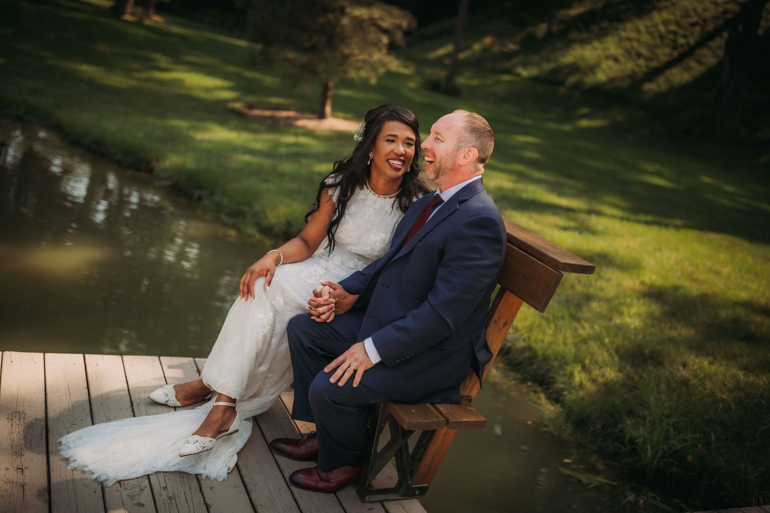 Newlyweds share intimate moments on a wooden dock by a tranquil lake.