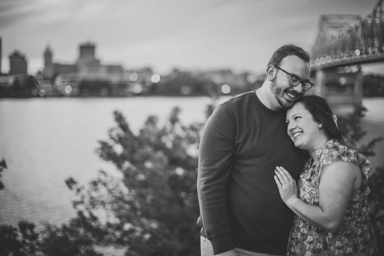 Black and white portrait of couple sharing tender moment by waterfront at dusk.