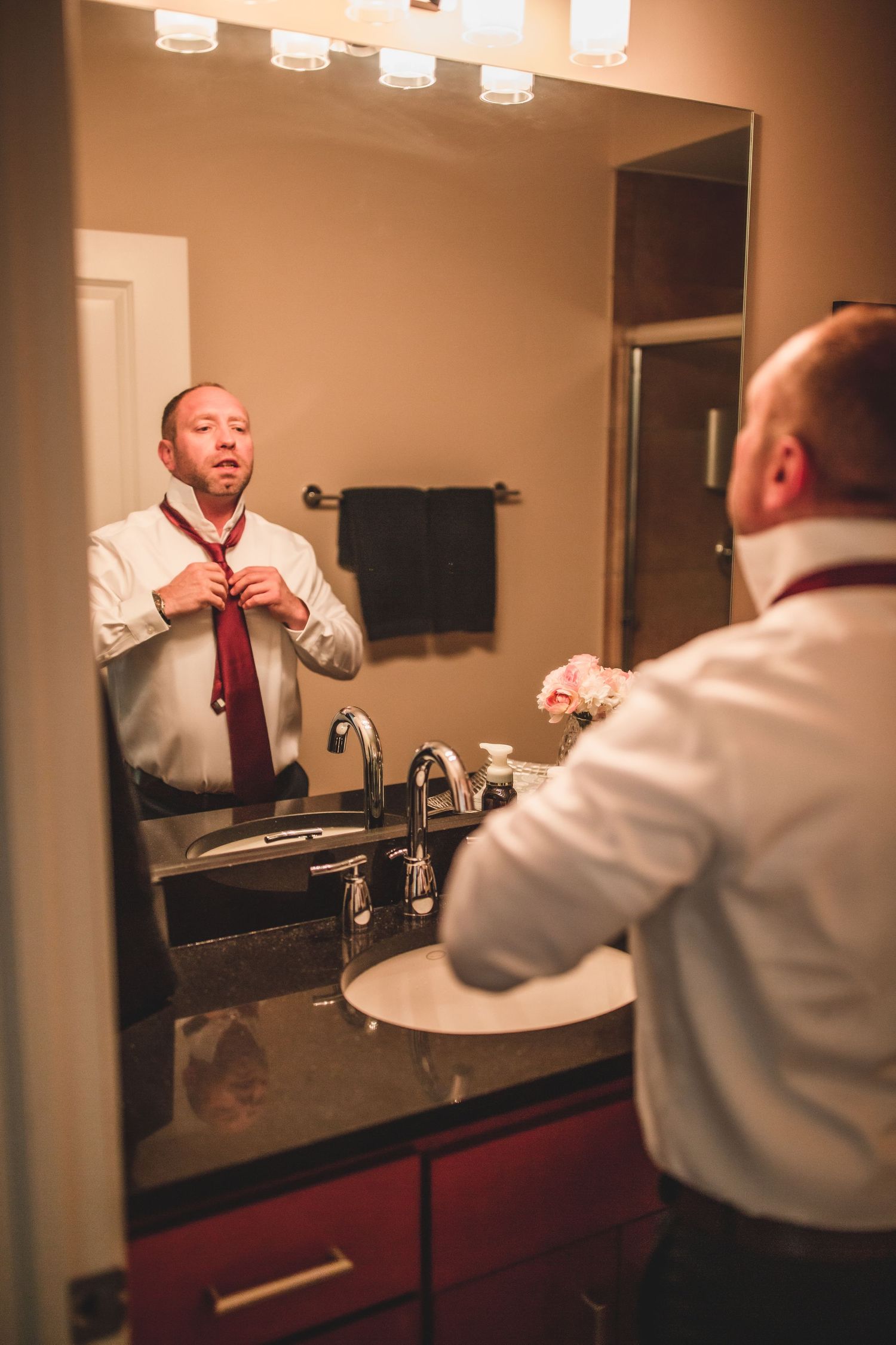 Person adjusting tie while looking in bathroom mirror with vanity lighting.