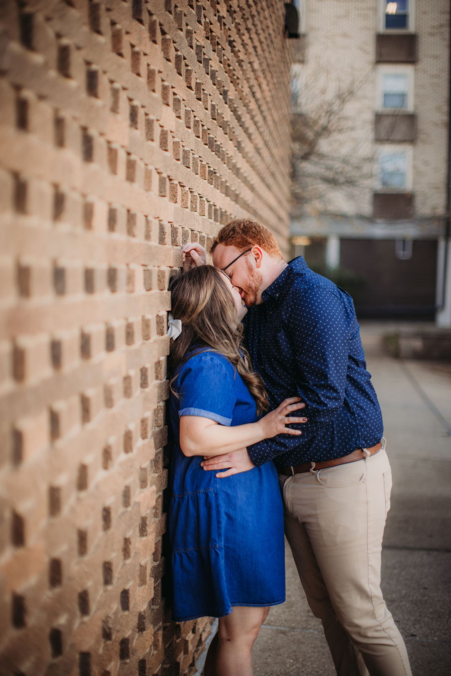 Couple sharing an intimate moment beside a patterned brick wall.