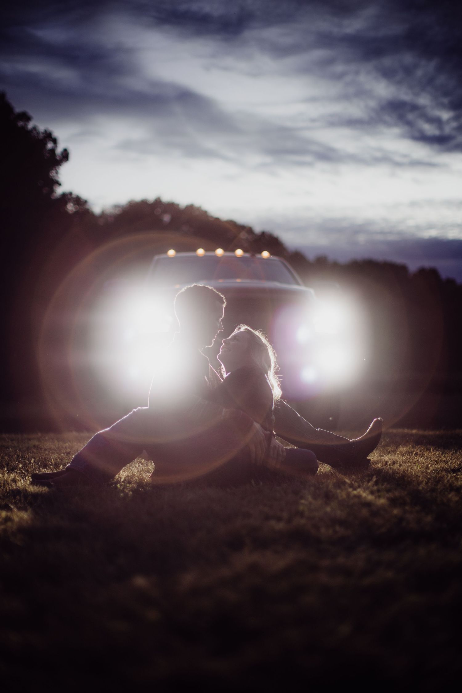 Silhouetted couple sitting in a field at sunset with dramatic lens flare creating a romantic atmosphere.
