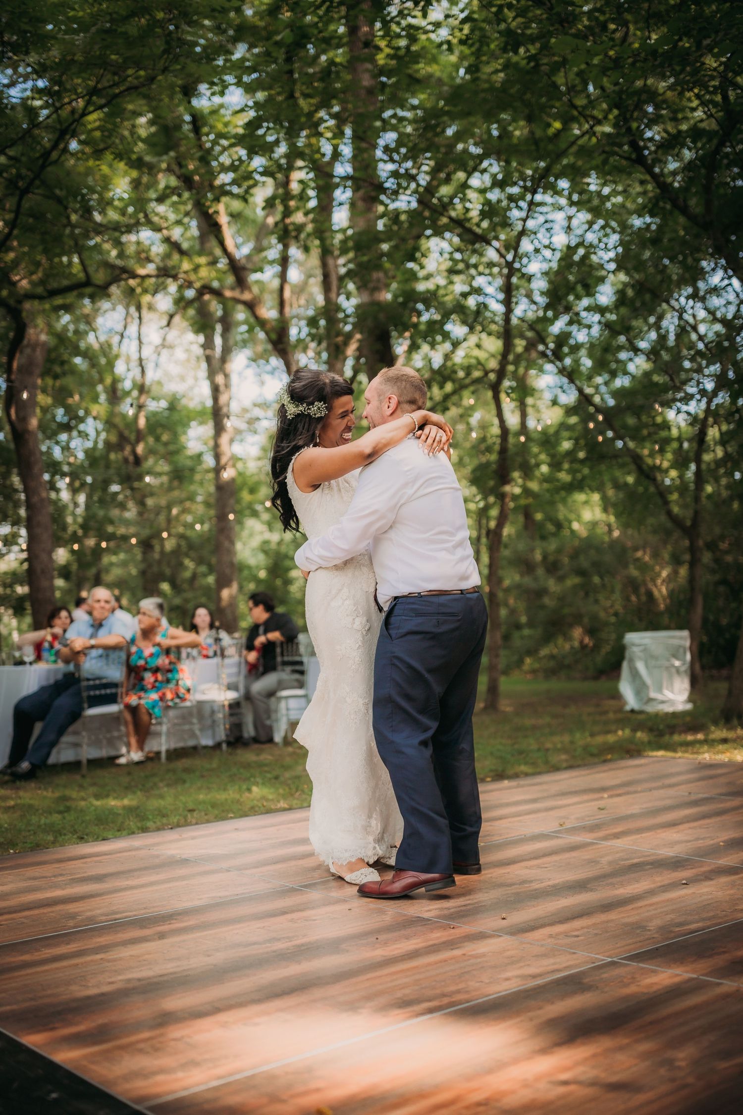 Newlyweds share an intimate dance moment on a wooden platform during their outdoor forest reception.