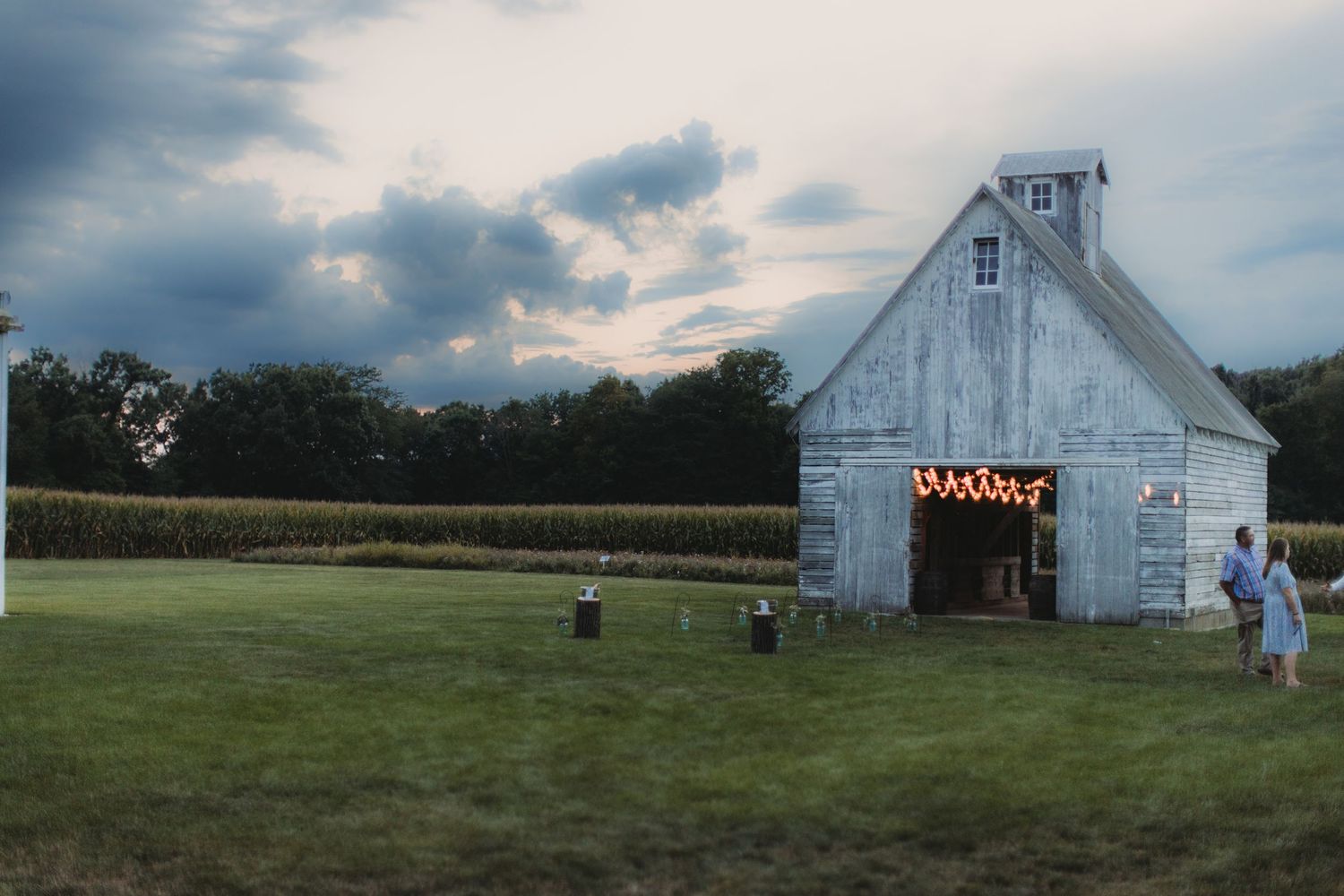 White farm barn with scenic countryside field and cloudy sky background.
