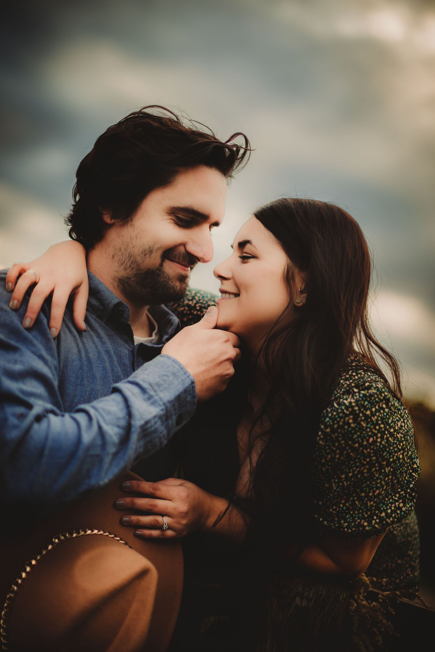 Couple sharing a romantic moment outdoors at sunset with a brown felt hat visible.