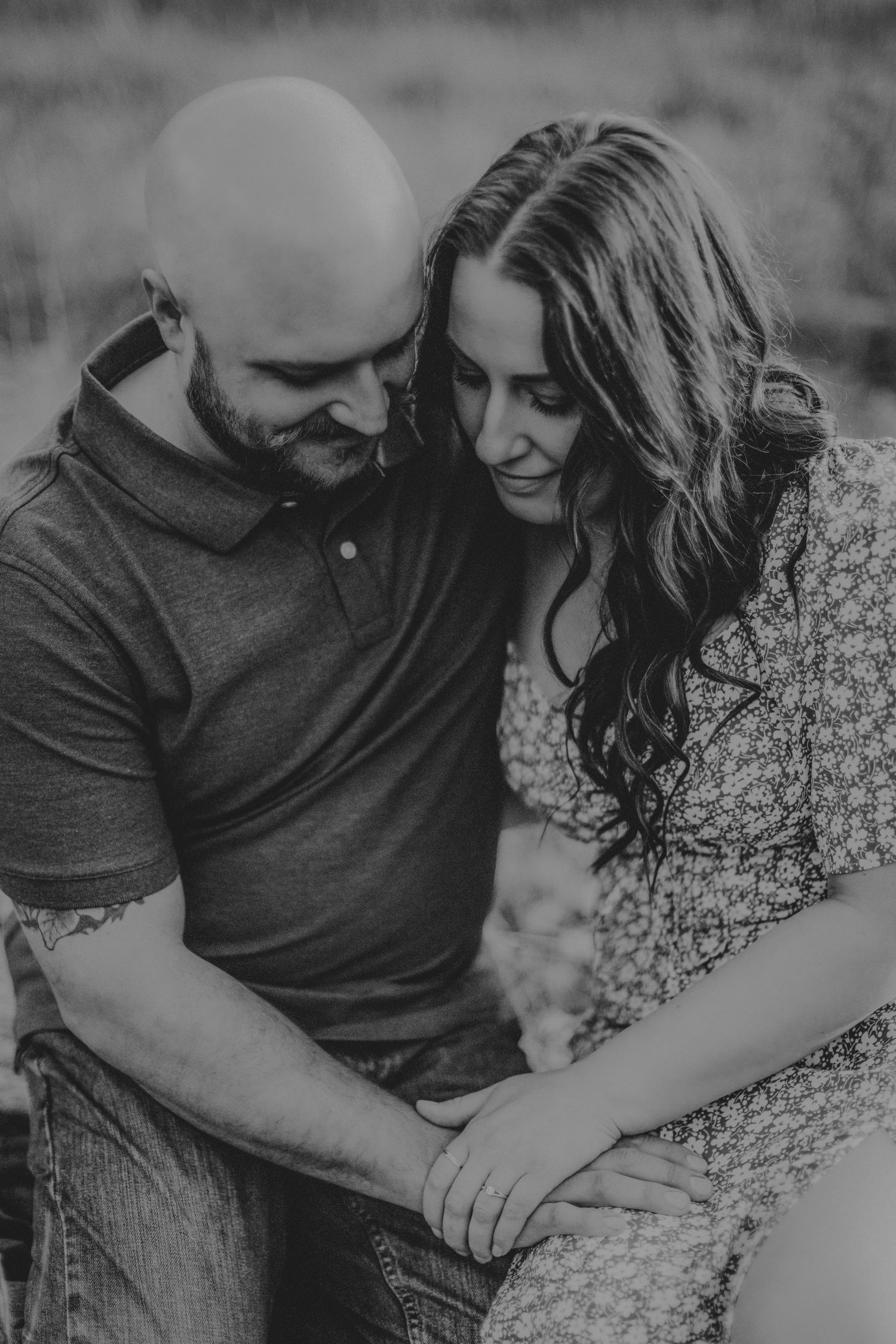 A black and white portrait of a couple sharing an intimate moment while sitting together outdoors.