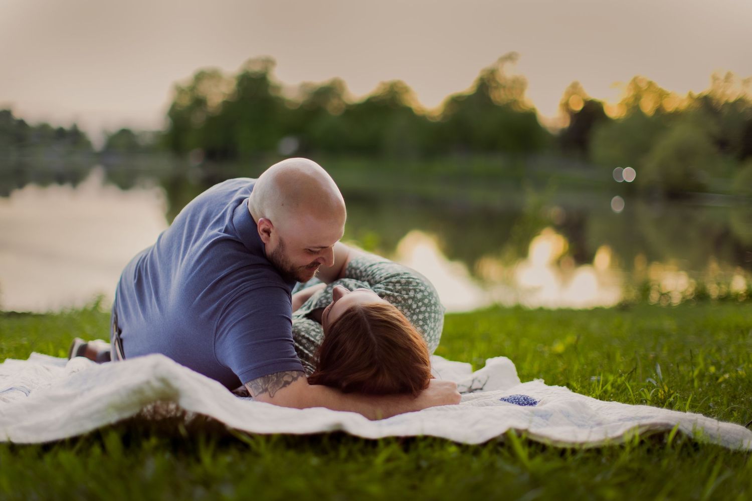 Couple sharing tender moments on a white blanket during an outdoor photoshoot.