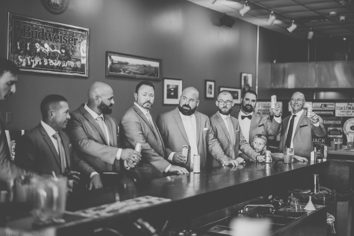 Group of formally dressed people gathered at bar counter in black and white photo.