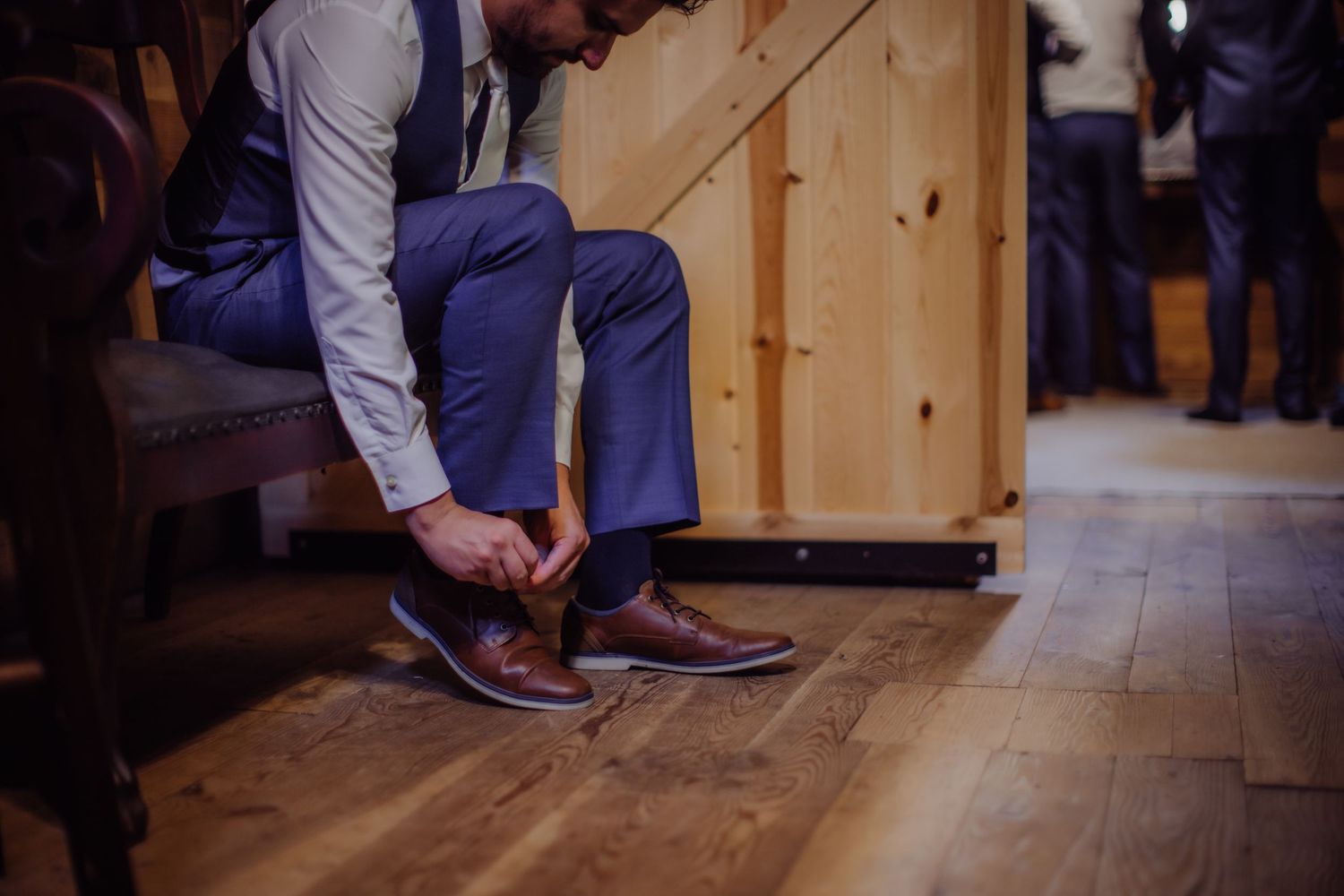 Close-up of person tying brown leather dress shoes on wooden floor.