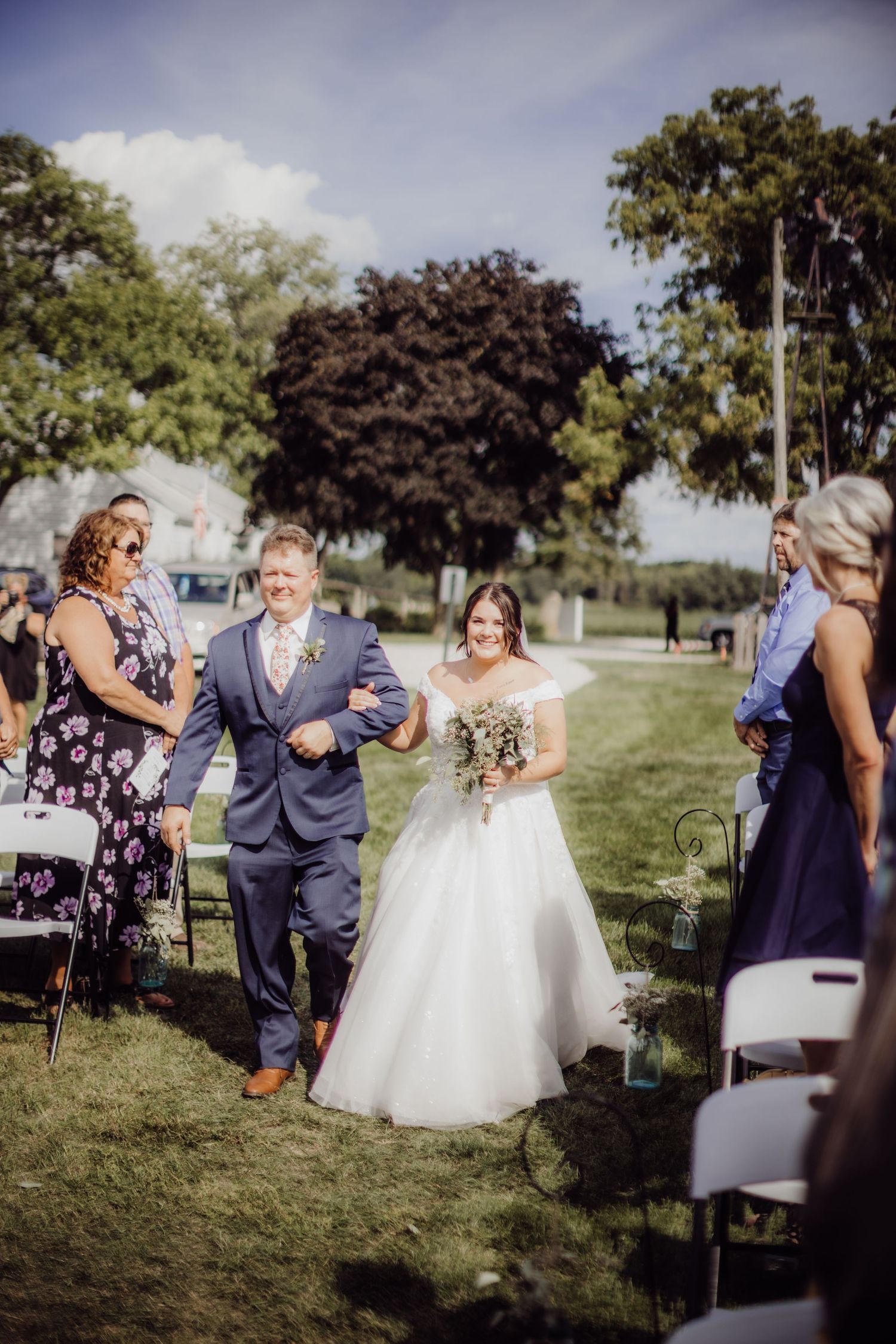Wedding celebration candid moments on grassy field with guests and formal attire.