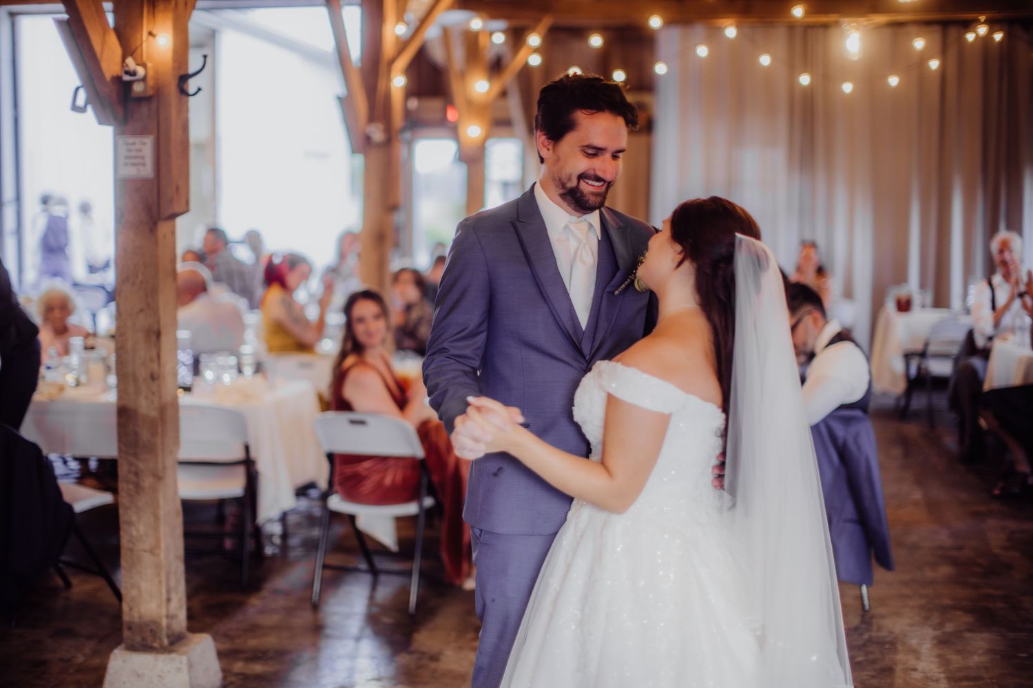 Happy couple shares their first dance in a rustic barn reception venue with wooden beams.