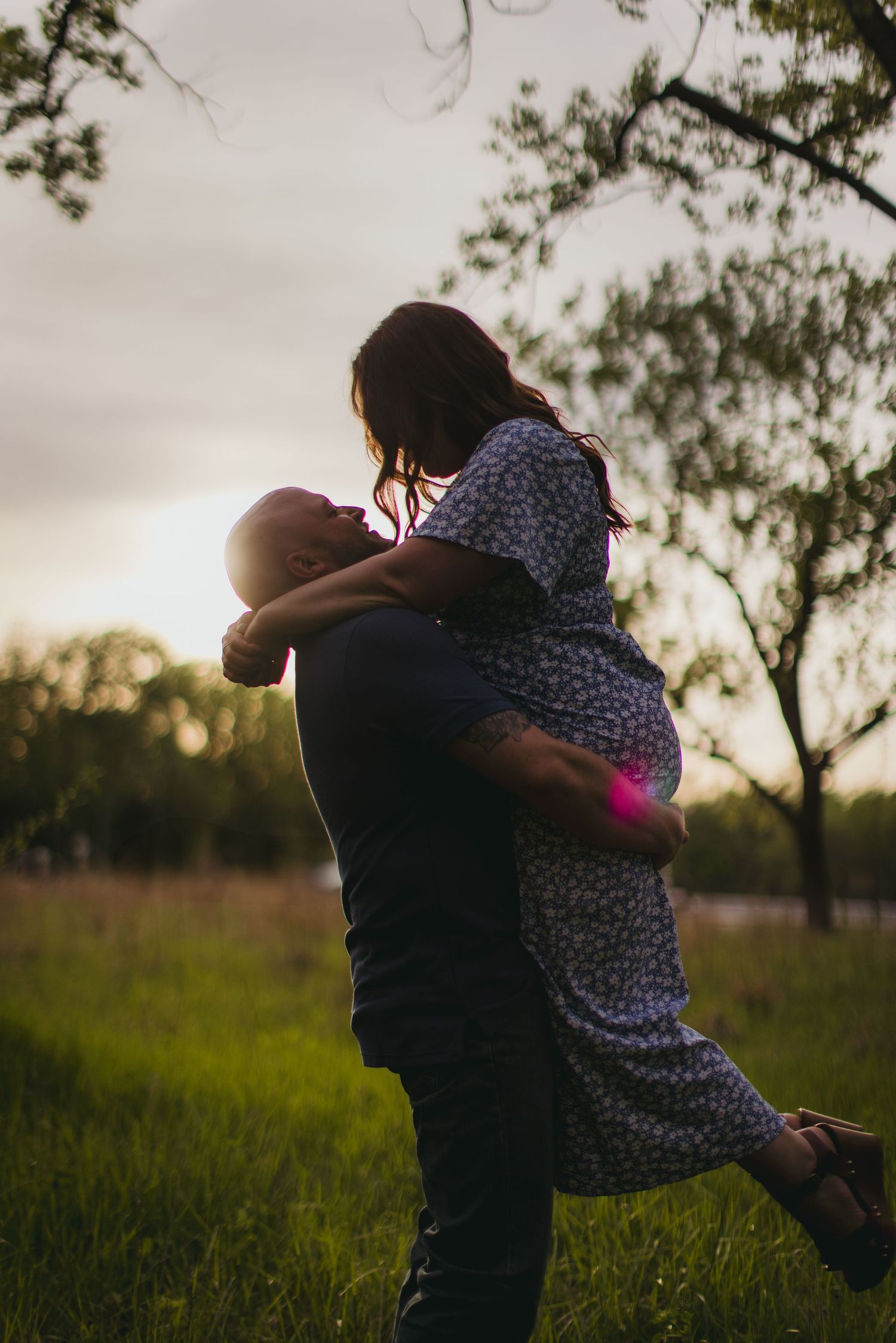 Sunset silhouette of a couple spinning in an embrace with golden light in background.