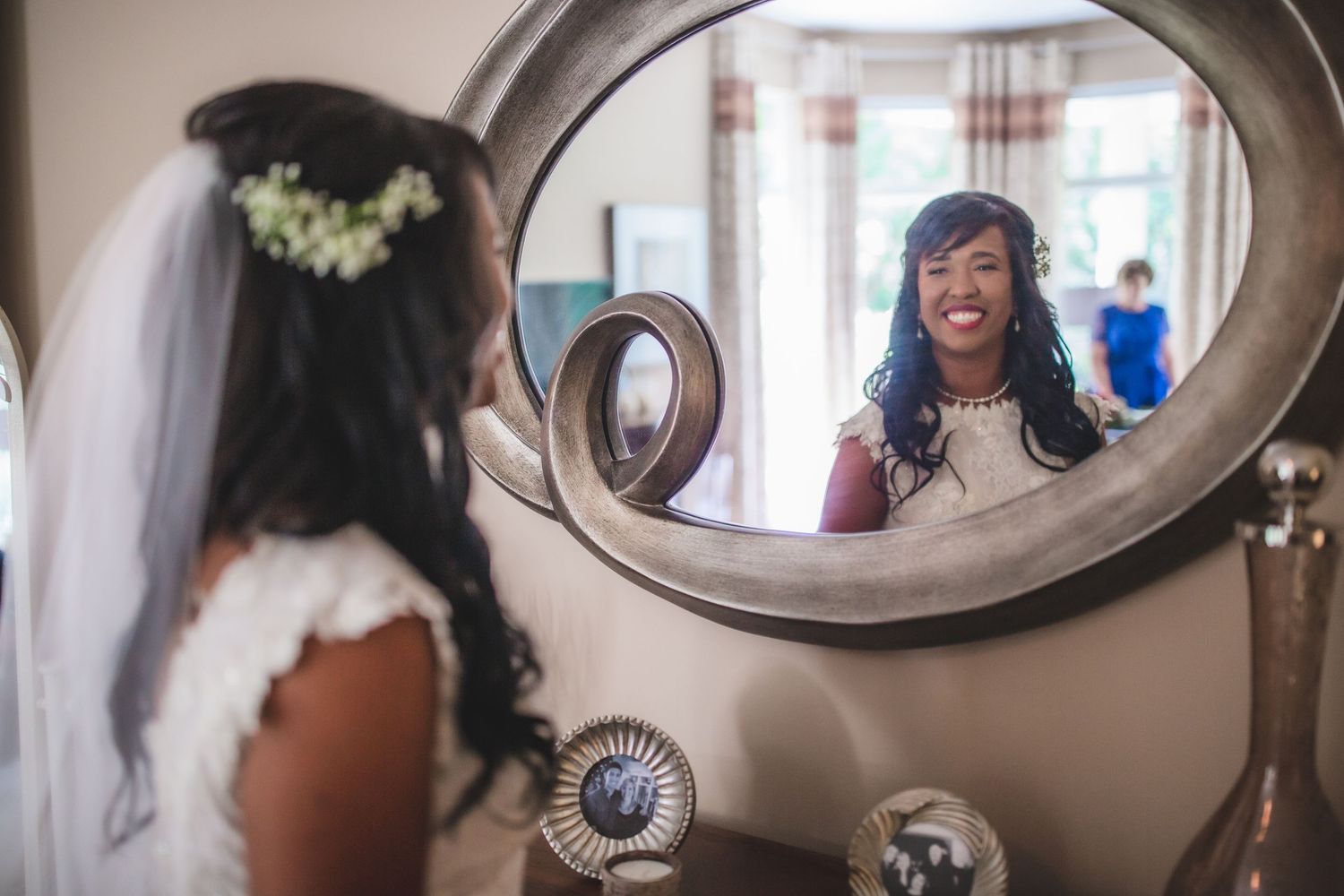 A radiant bride sees herself in an oval mirror while preparing for her wedding ceremony.