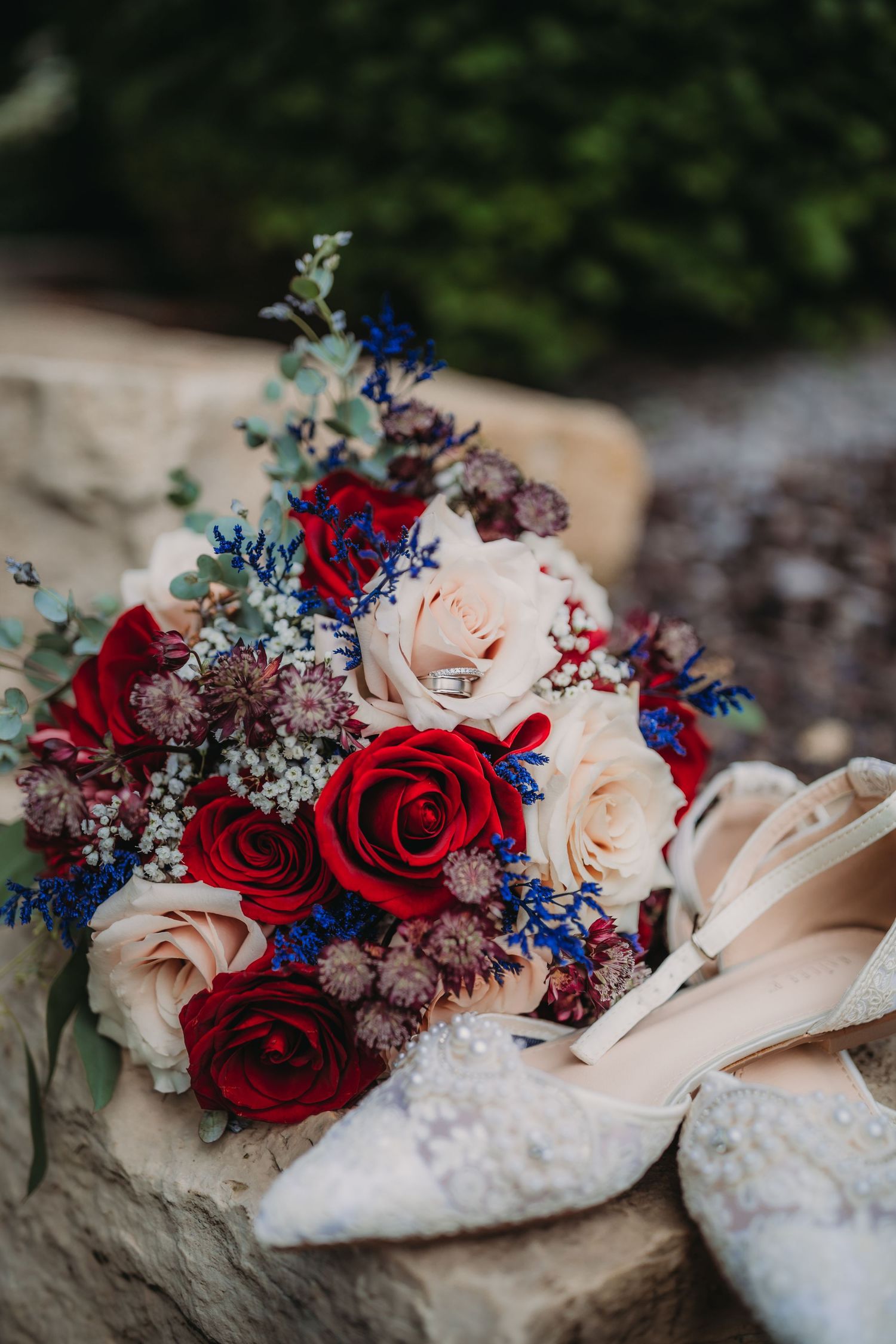 Detailed shot of patriotic wedding bouquet with roses and delicate lace shoes on stone.