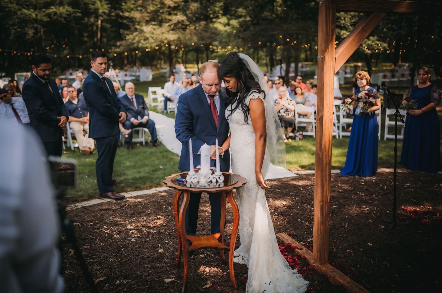 Outdoor wedding ceremony under wooden arbor with natural mulch ground covering.