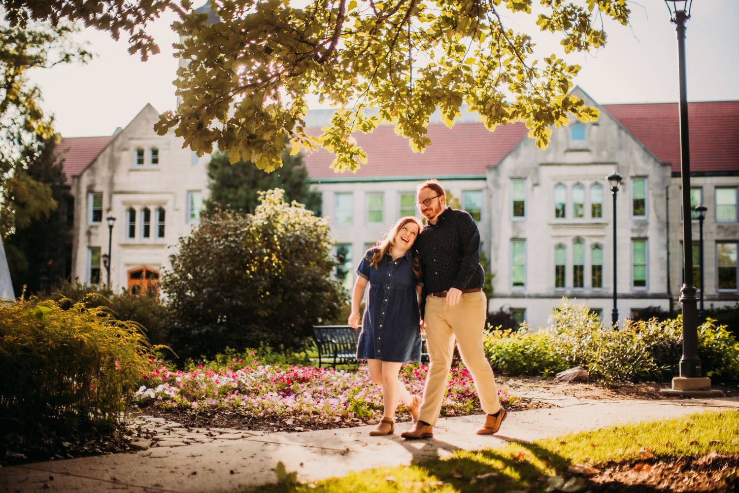 A couple walks together on a path with historic university buildings in the background.