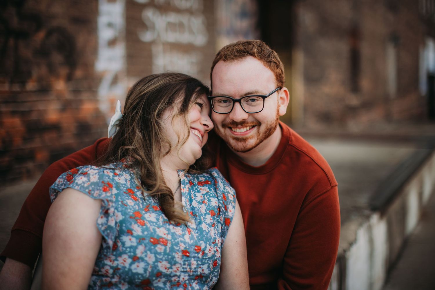 A couple shares an intimate moment by a brick wall with graffiti.