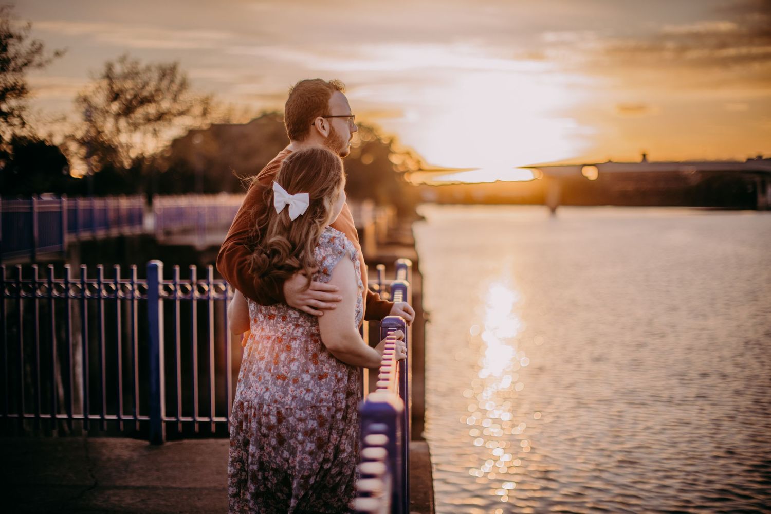Romantic waterfront sunset with couple embracing along metal railings.