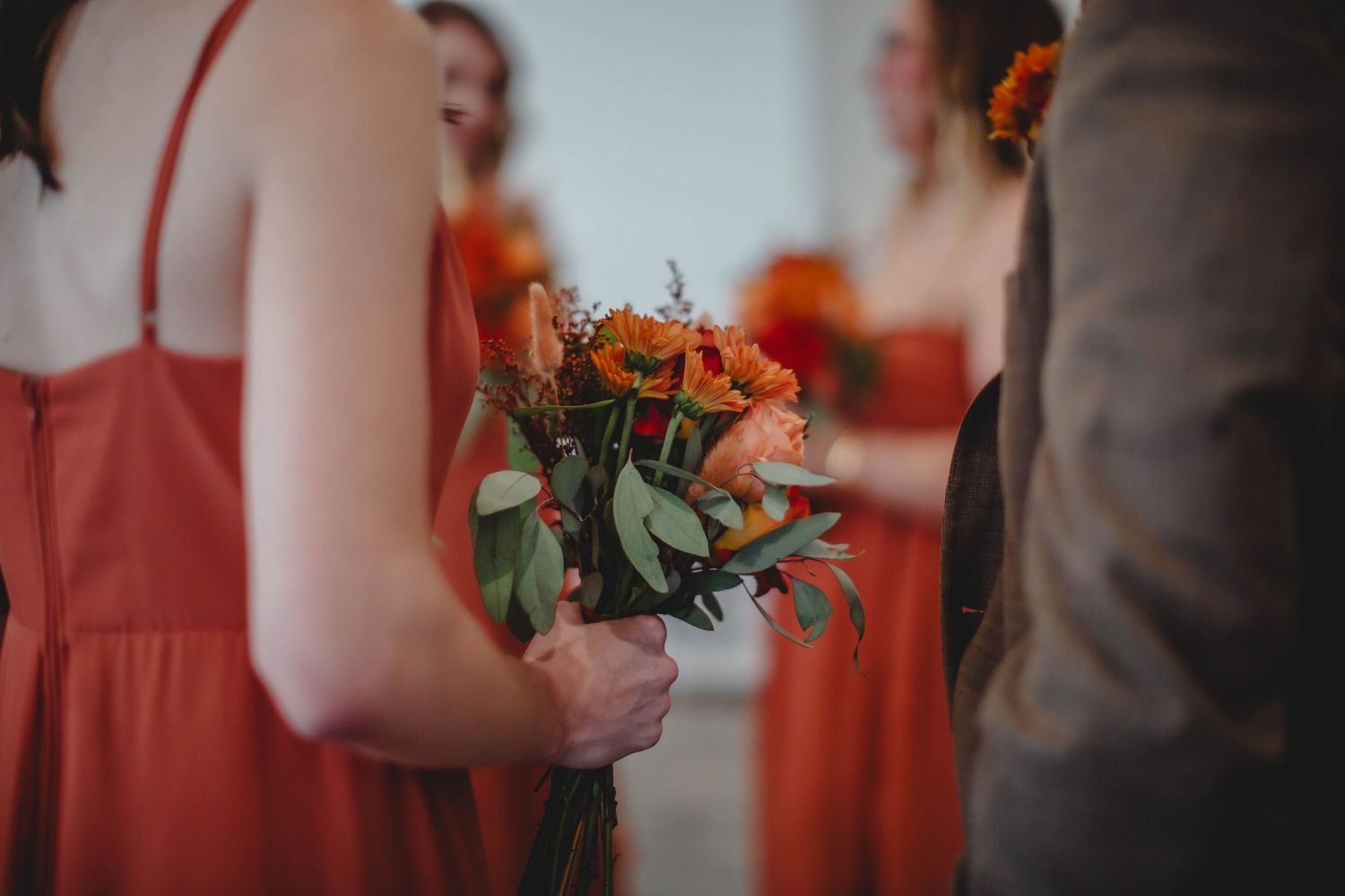 A close-up shot of a bridesmaid holding an orange and green bouquet.