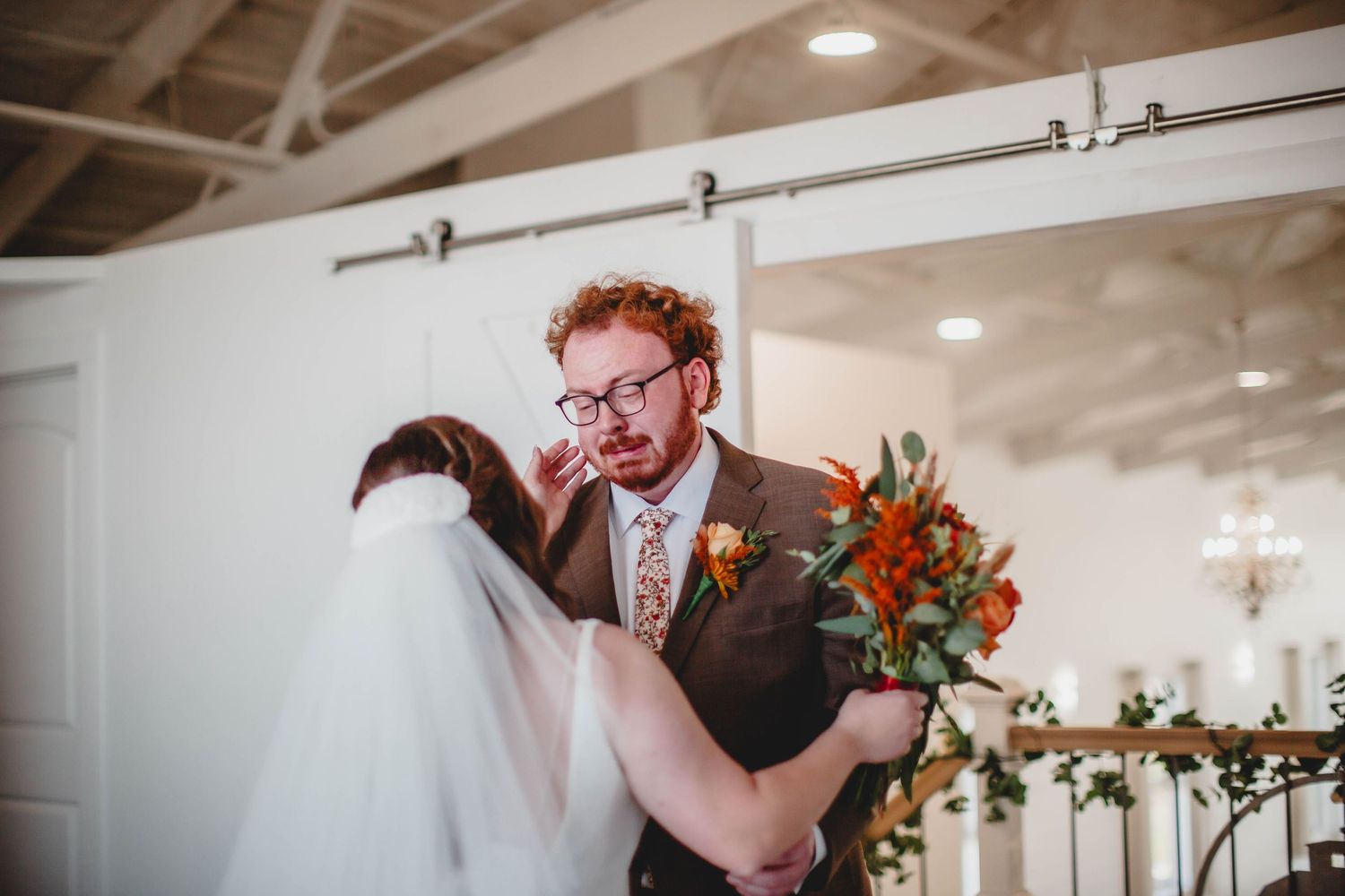 Emotional first look between newlyweds with vibrant orange and red wedding flowers.