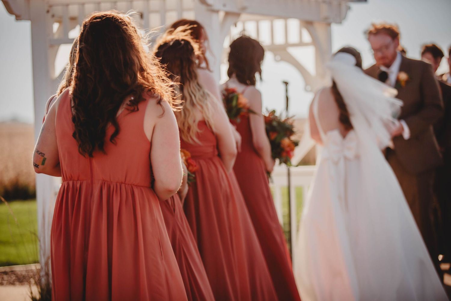 Bridesmaids in coral dresses watch ceremony from behind.